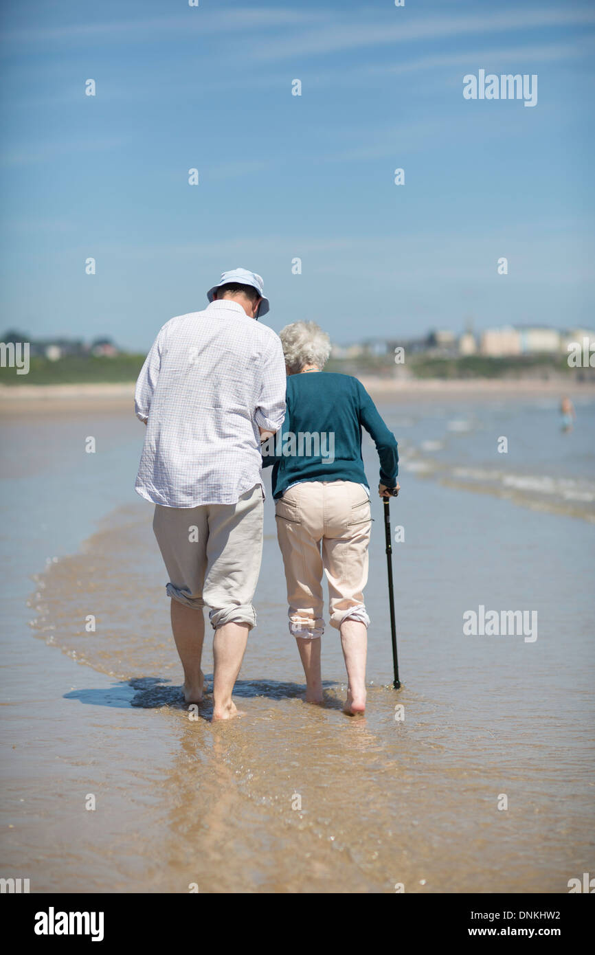 Eine ältere Frau Paddel entlang der Küste, unterstützt von einem Stab und einem Mann. Stockfoto