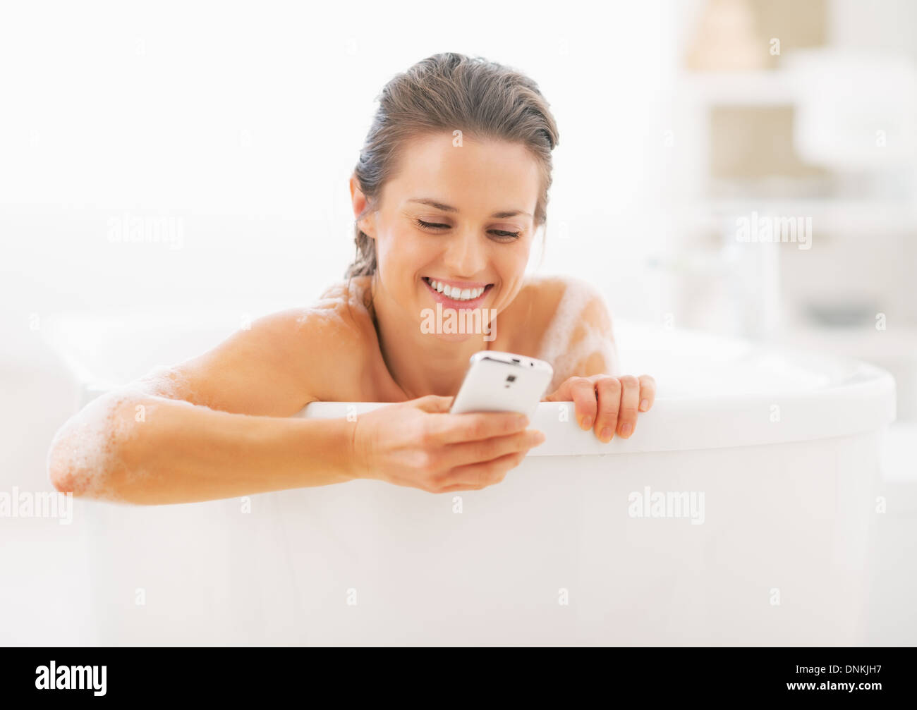 Lächelnde junge Frau schreiben Sms in Badewanne Stockfoto