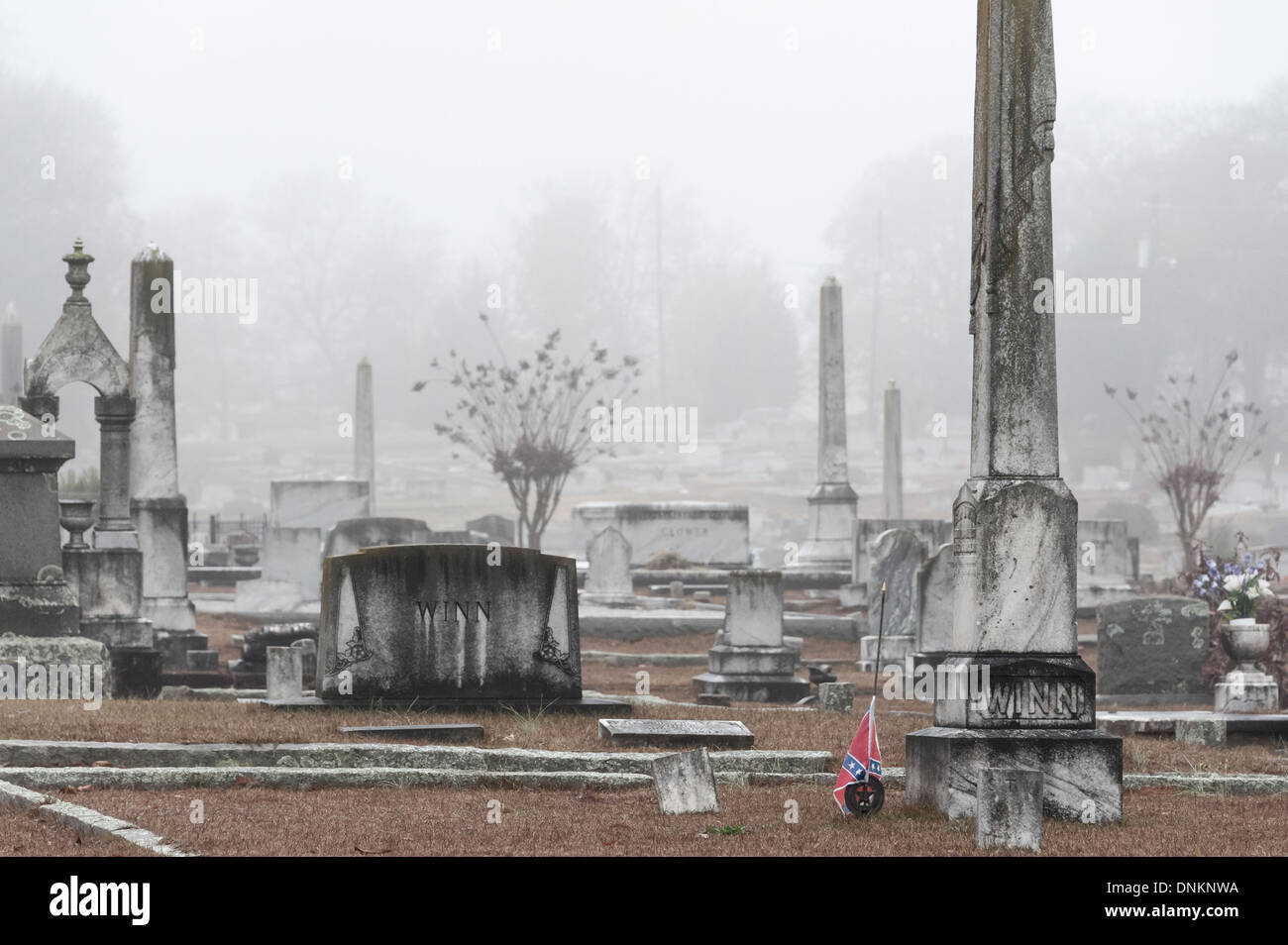 Eine Medaille und eine Flagge der konföderierten Veteranen begleiten einen Grabmarker auf einem nebelumhüllten Friedhof in Lawrenceville, Georgia. (USA) Stockfoto