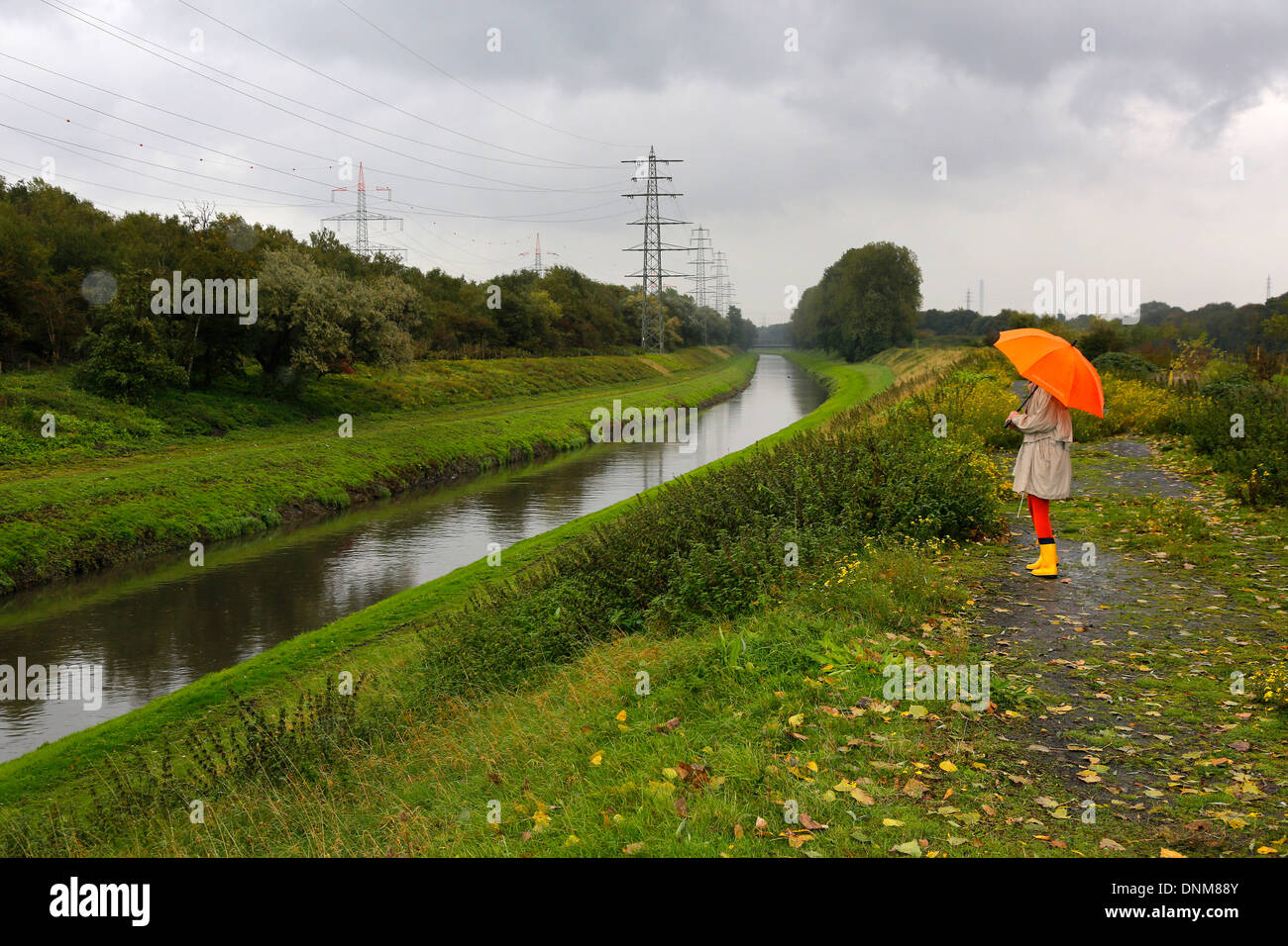 Oberhausen, Deutschland, geht eine junge Frau im Regen mit Regenschirm zu Fuß entlang der Emscher Stockfoto