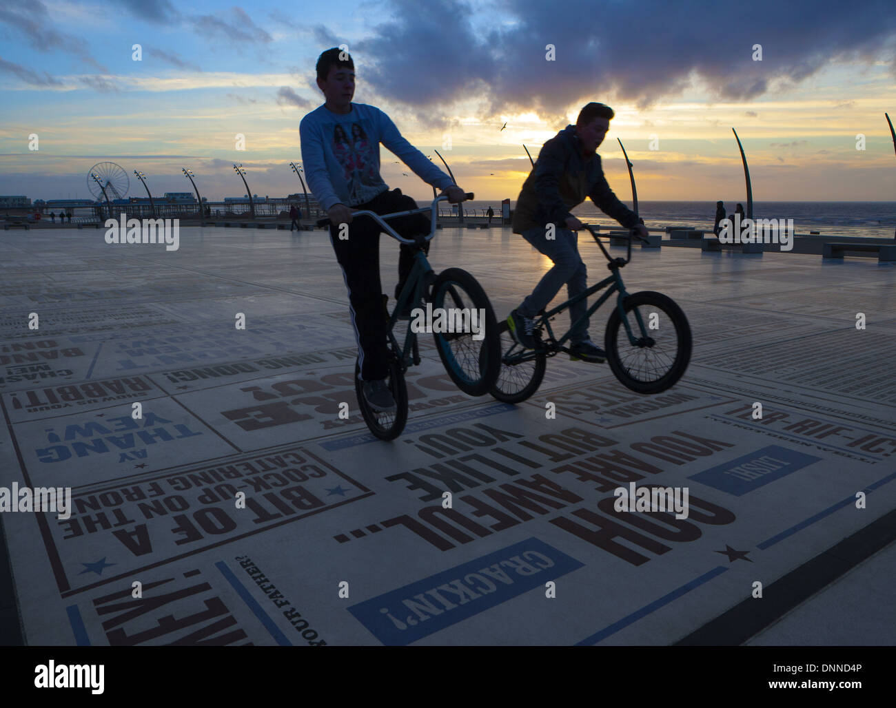 Jungs im Teenageralter Fahrrad Kunststücke auf dem Blackpool Komödie Teppich oder Pflaster bei Sonnenuntergang. Lancashire, UK Stockfoto