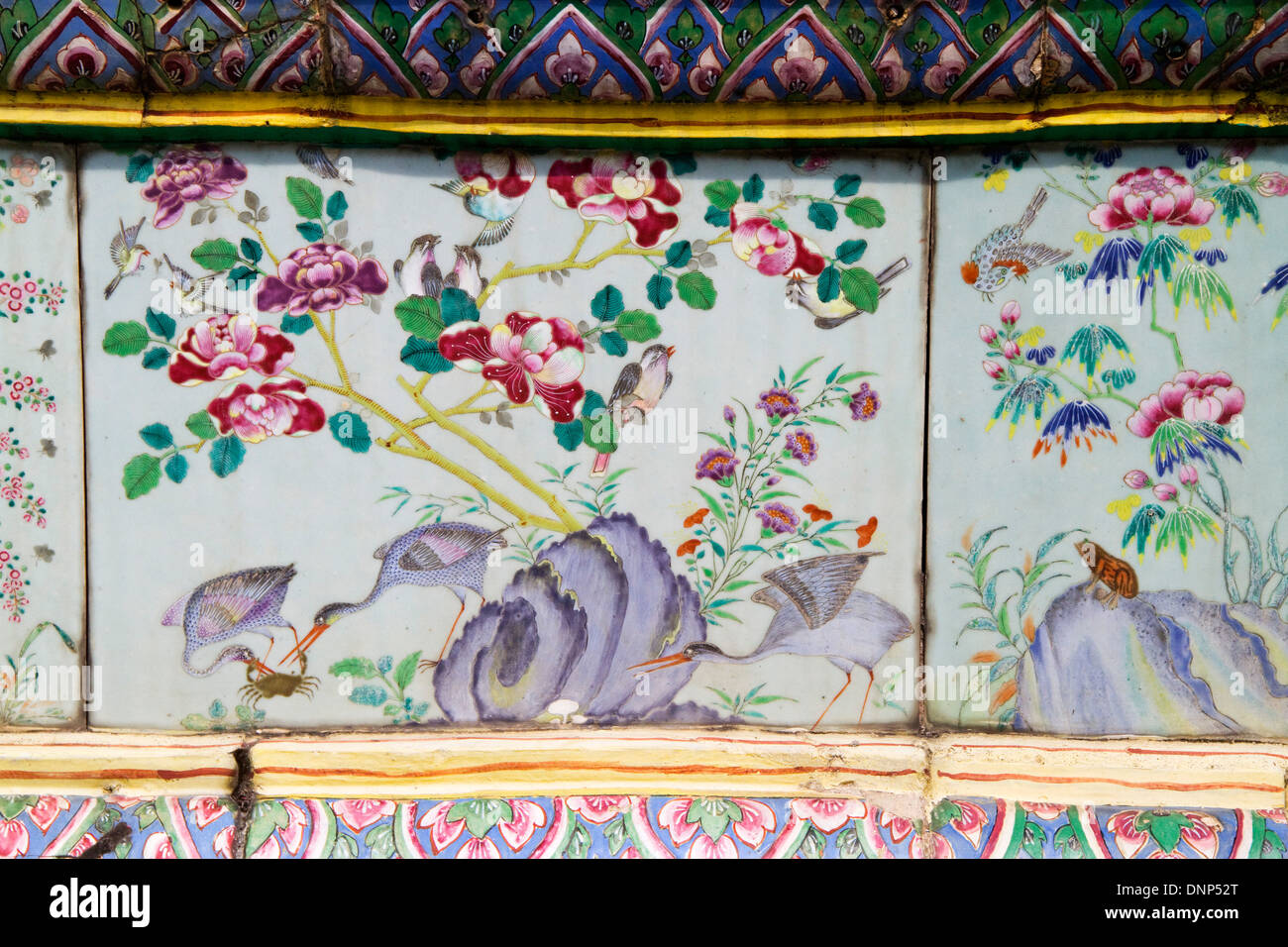 Vögel und Blumen zieren handgemalte keramische Platten, die einige der Wände in den Grand Palace.Bangkok,Thailand säumen. Stockfoto