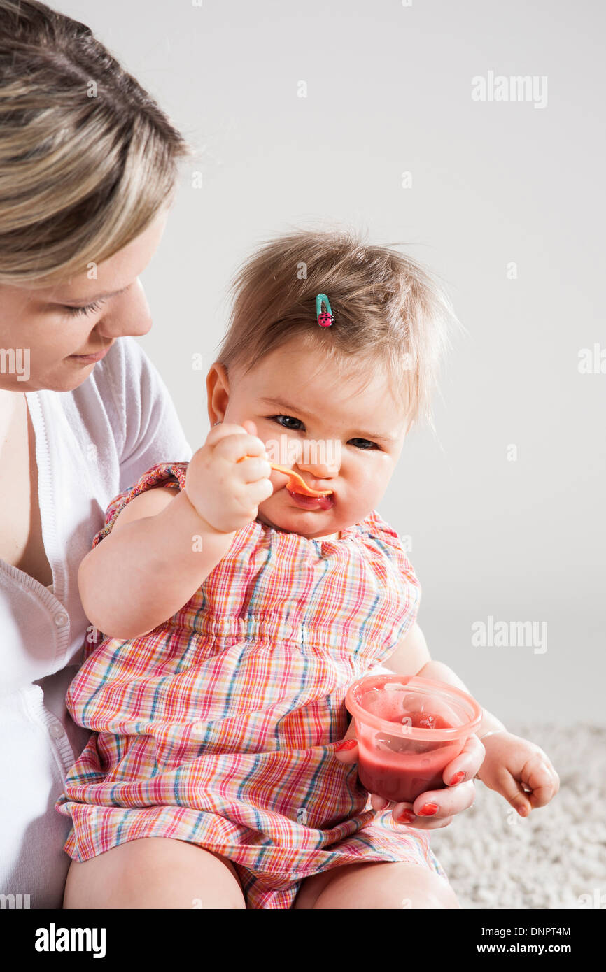 Porträt von Baby Girl Fütterung selbst auf Mutters Schoß, Studioaufnahme Stockfoto