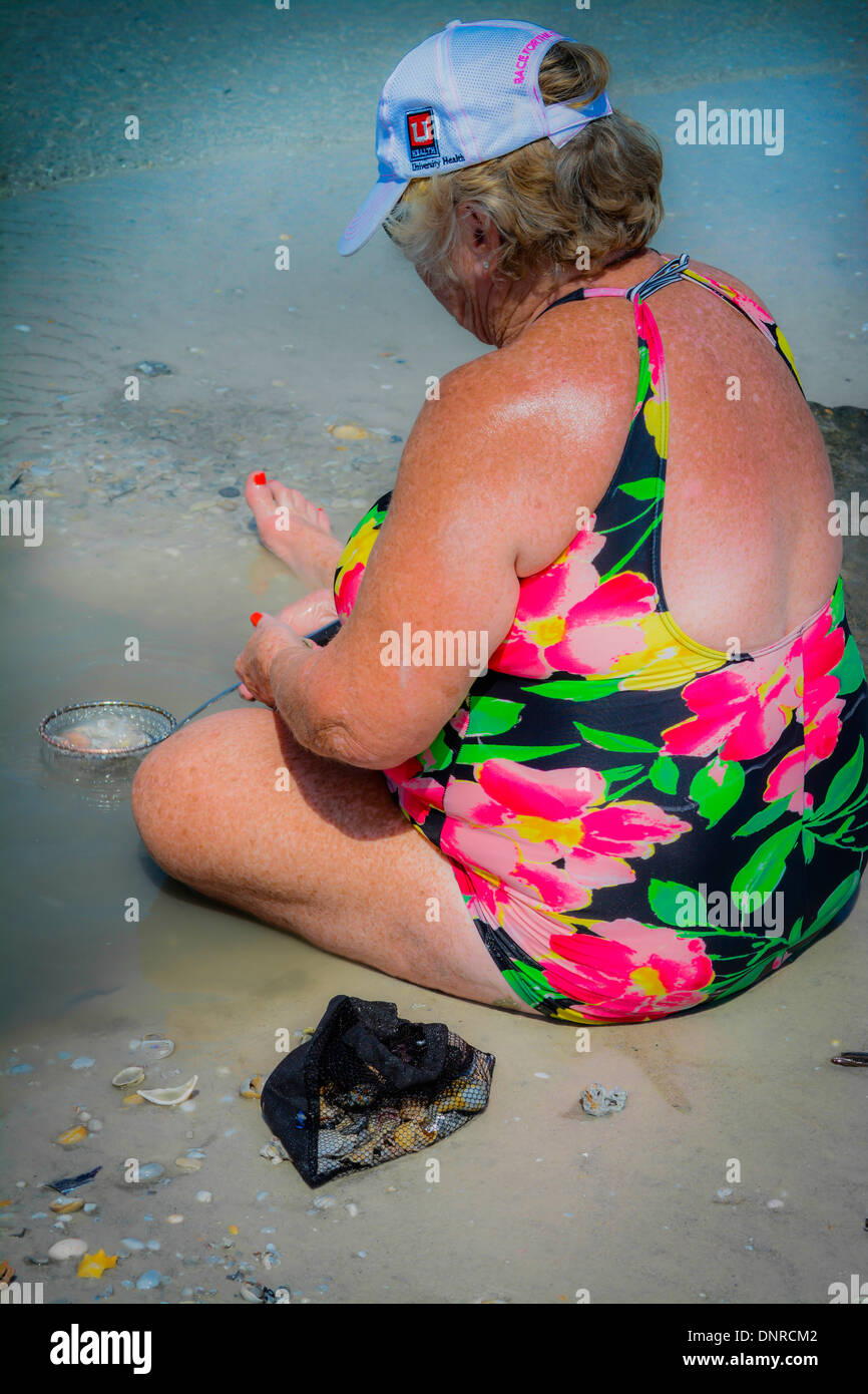Über der Schulter eine ältere weiße Frau alleine am Strand sitzen, wie sie für Pfannen Haie Zähne Stockfoto