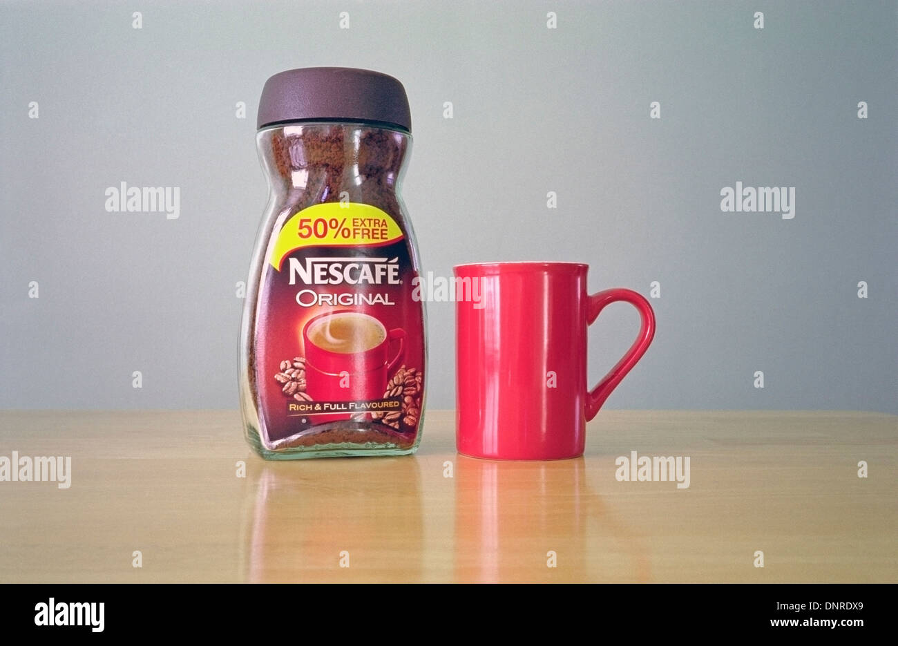 Glas mit Nescafe Instant Kaffee Granulat mit einem roten Becher Stockfoto
