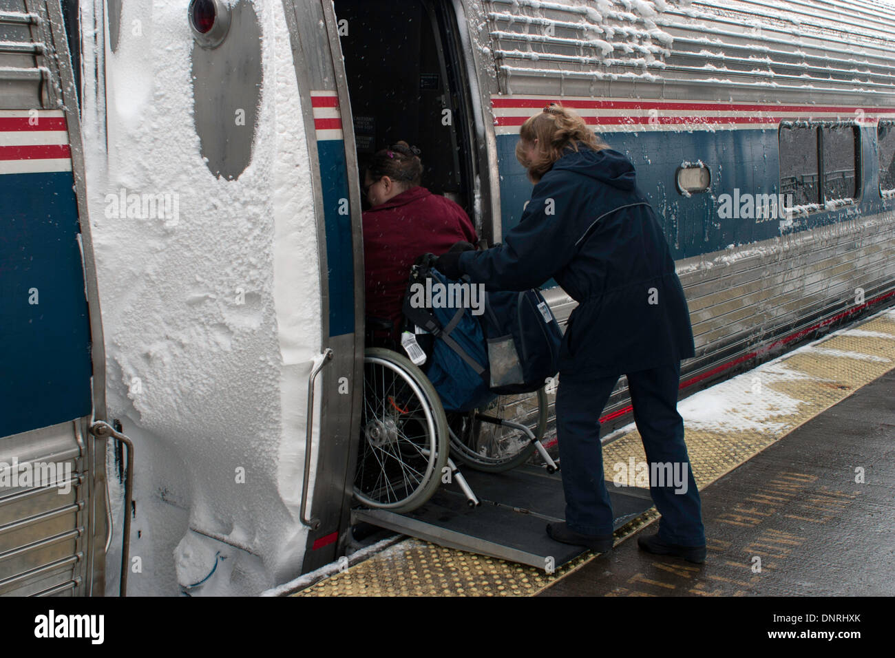 Angestellter Amtrack hilft ein Passagier-Board der Zug an einem stürmischen Wintertag. Stockfoto