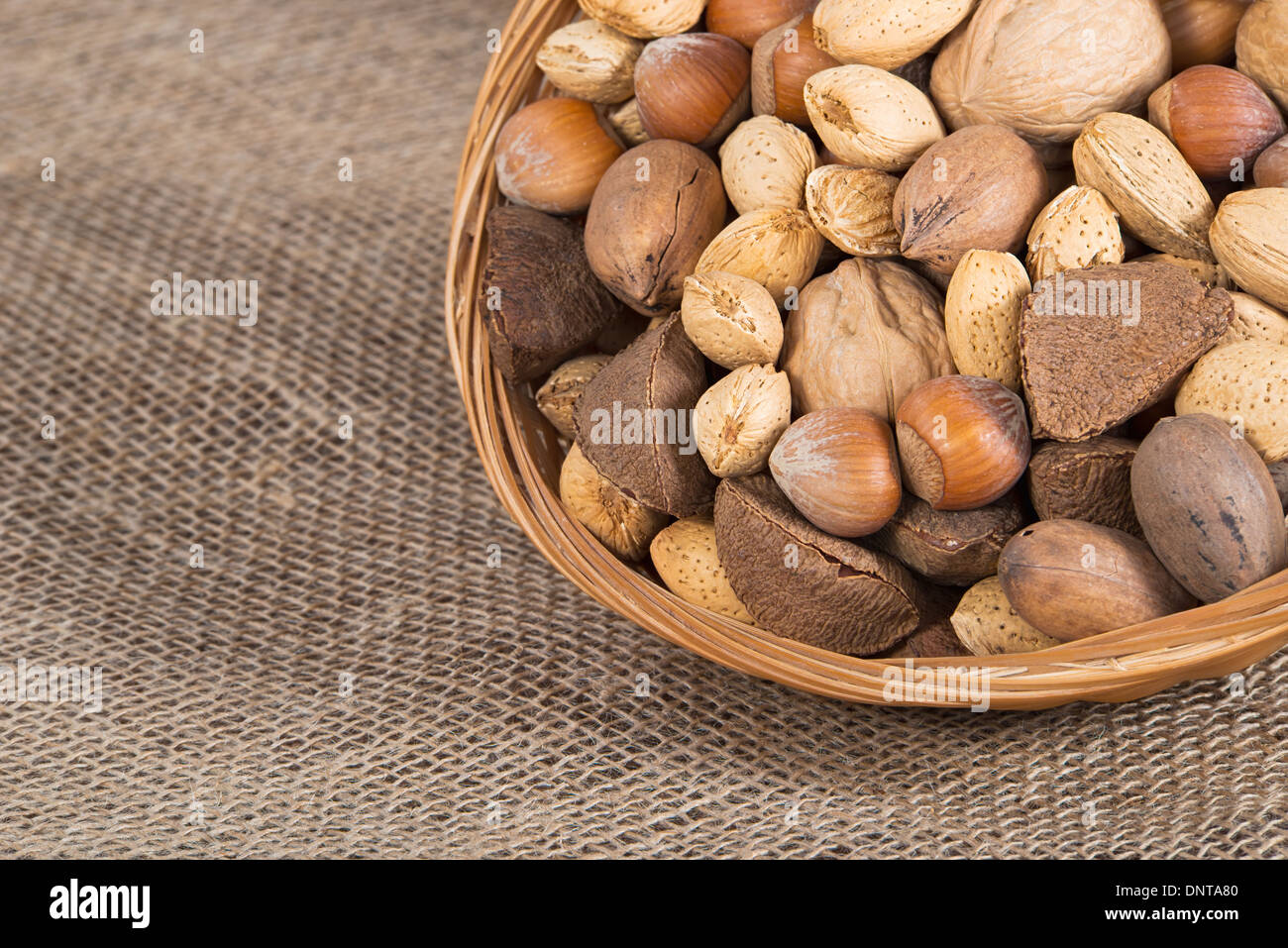 Gemischte Nuss-Korb mit Mandeln, Paranüsse, Haselnüsse, Walnüsse und Pekannüsse. Sackleinen Hintergrund mit Textfreiraum. Stockfoto