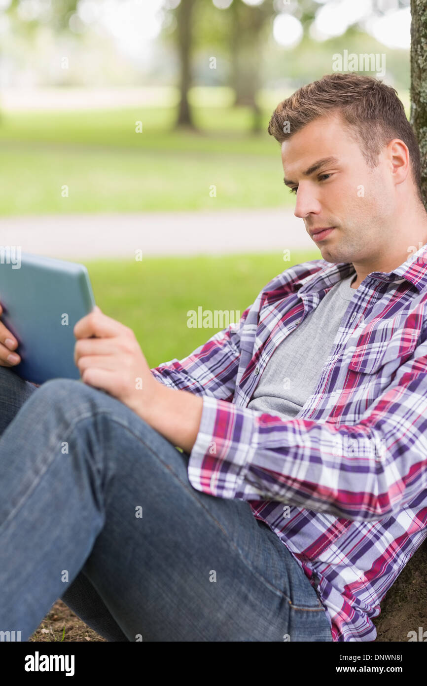 Ernsthaften Studenten mit seinem Tablet-pc außerhalb stützte sich auf Baum Stockfoto