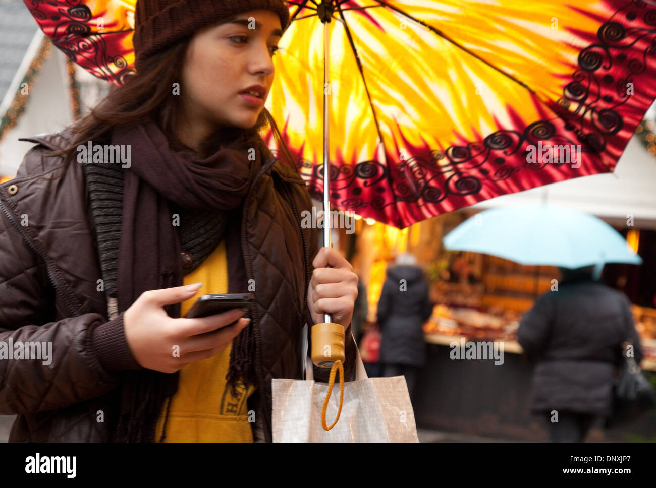 Ängstlich attraktive junge Frau in einem Ansturm, SMS auf ein Handy, und hält einen bunten Regenschirm, Köln, Deutschland, Europa Stockfoto