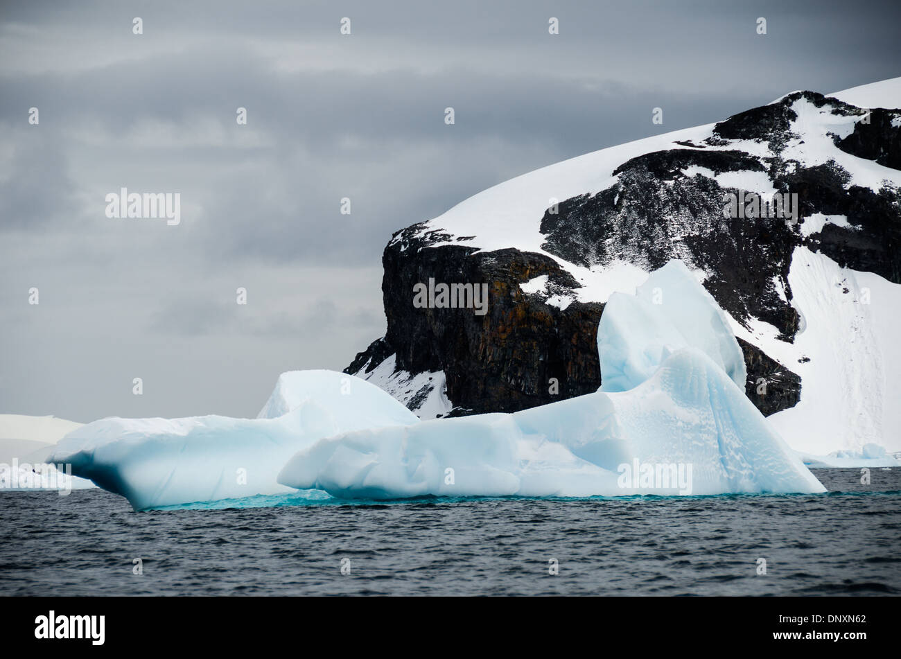 Eisberge Trinity Island Antarktis // die weichen Formen einiger vorbeiziehender Eisberge stehen im Kontrast zu den rauen Kanten der Klippen des Berges im Hintergrund auf Trinity Island, Antarktis. Stockfoto