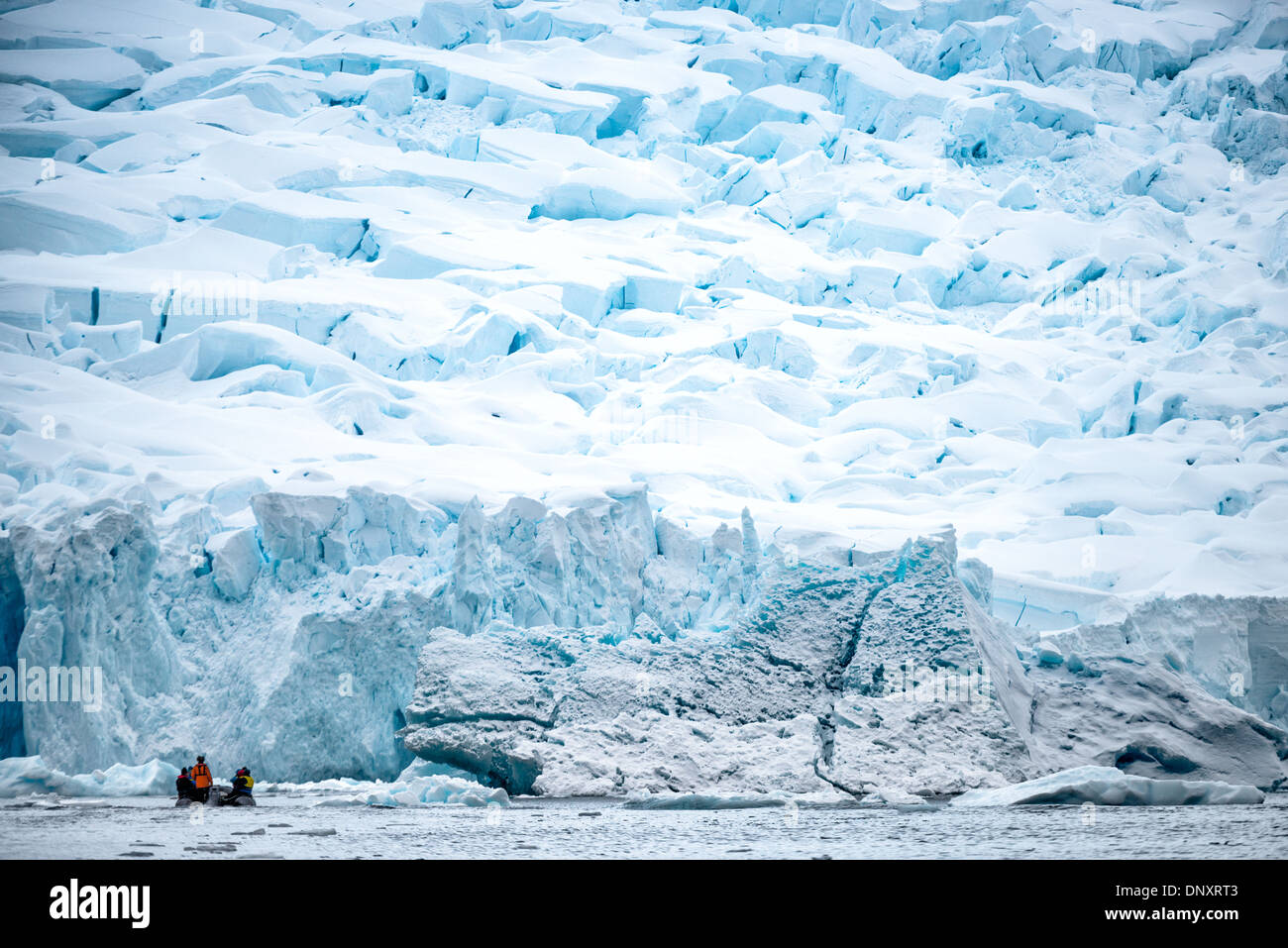 Antarktis - Touristen in ein Zodiac Schlauchboot Kreuzfahrt vorbei an steilen Klippen von Eis von einem Gletscher am Ufer am Curtis Bay auf der Antarktischen Halbinsel. Stockfoto