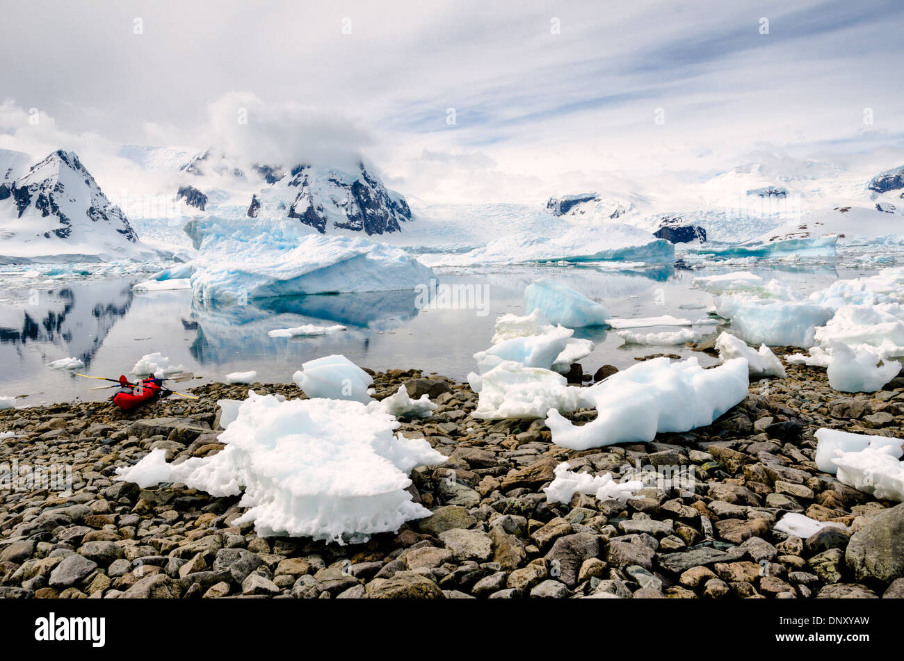 Eine Kajak ist am felsigen Strand von Cuverville Island auf der antarktischen Halbinsel, mit den Bergen im Hintergrund reflektiert auf dem ruhigen Wasser hochgezogen. Stockfoto