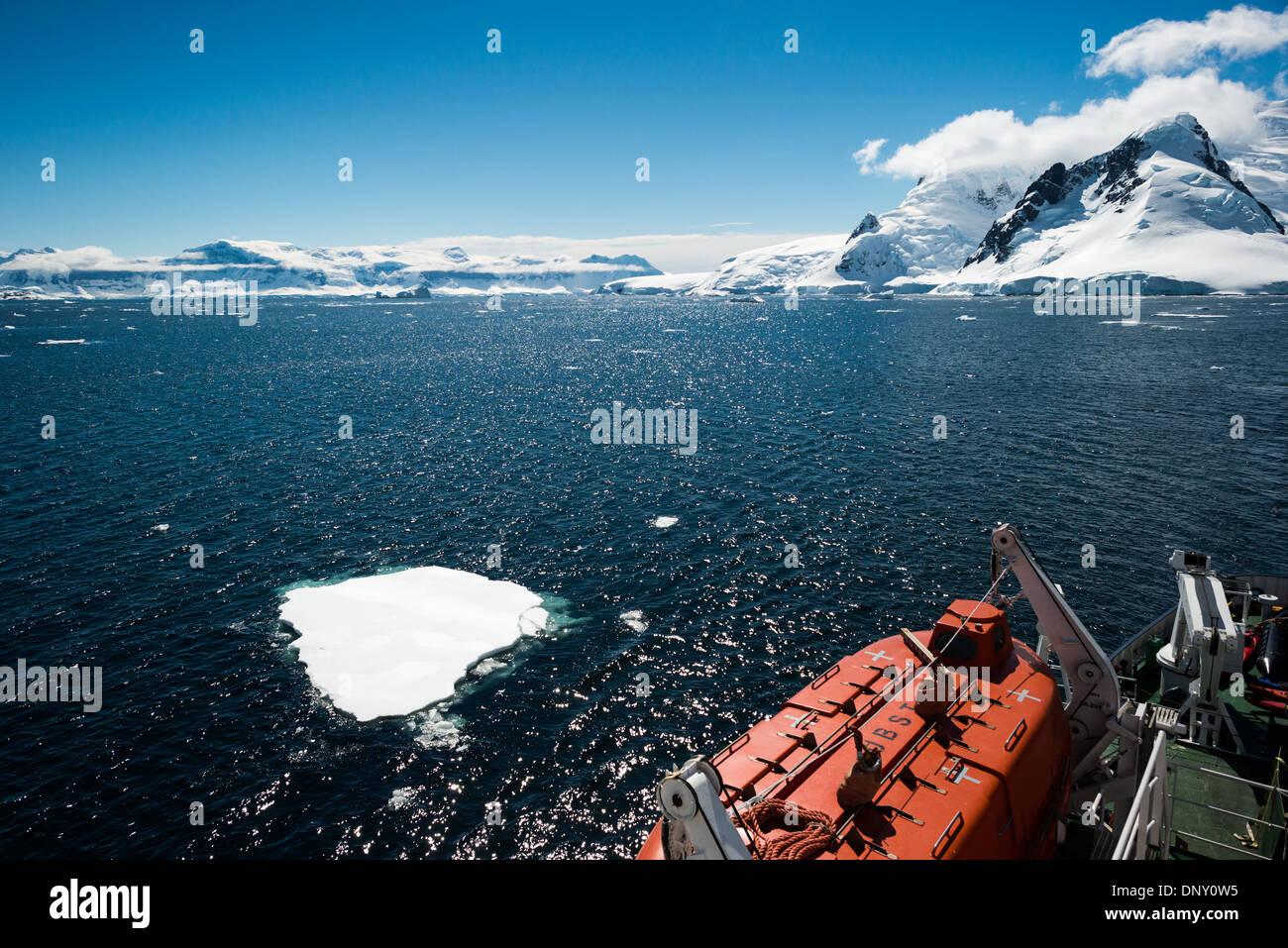 Antarktis - ein Kreuzfahrtschiff fließt durch einen Kanal, vorbei an kleinen Eisbergen. Im Vordergrund unten rechts am Rahmen ist eines der rettungsboote des Schiffes. Stockfoto