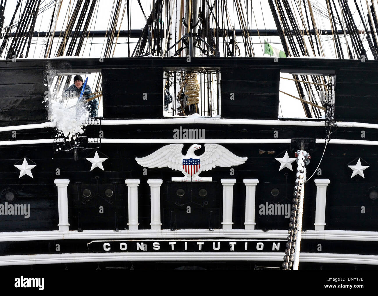 Ein US-Marine Seemann Schaufeln Schnee durch eines der Heckspiegel Pistole Häfen an Bord der großen Segelschiff die USS Constitution nach Winter Sturm Herkules, fast zwei Fuss Schneefall in der Gegend von Boston 3. Januar 2014 in Charlestown, Massachusetts links. Stockfoto