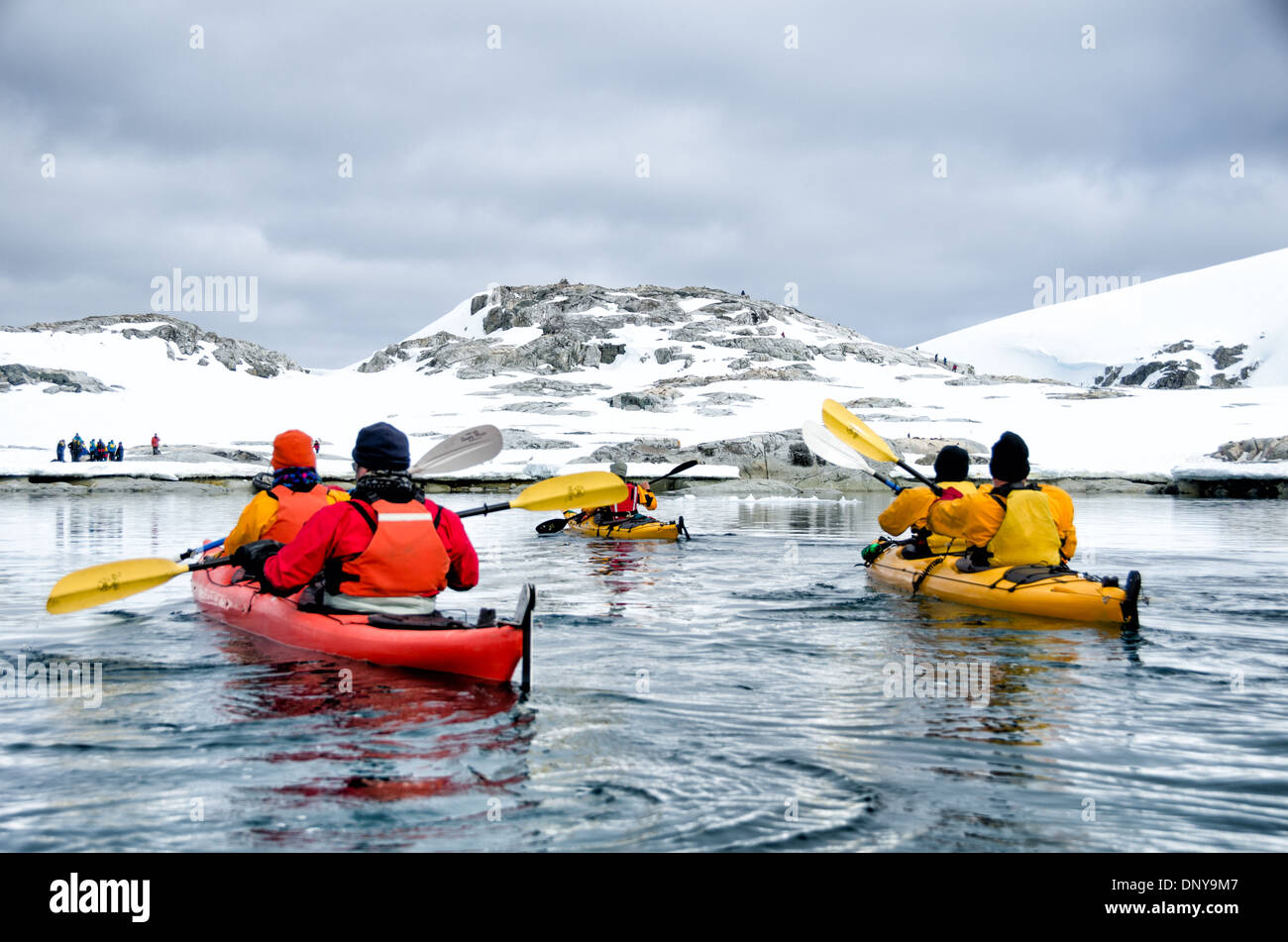 Antarktis - Kayaker paddeln entlang der glasigen Bedingungen neben malerischen Bergen an der Küste in der Nähe von Petermann Island an der Westküste der Antarktischen Halbinsel. Stockfoto