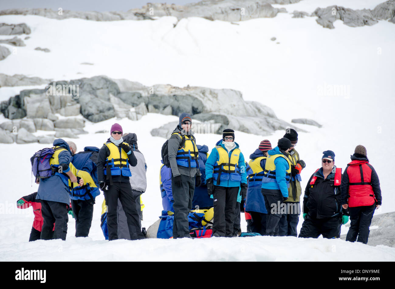 Antarktische Touristen Petermann-Insel Antarktis | PETERMANN-INSEL, Antarktis — Eine Gruppe von Expeditionstouristen in Schwimmwesten wartet an Land auf der Petermann-Insel darauf, von Schlauchbooten des Typs Zodiac abgeholt und zurück zu ihrem Schiff gebracht zu werden. Die Petermann-Insel im Wilhelm-Archipel südlich des Lemaire-Kanals ist einer der meistbesuchten Anlegeplätze an der westlichen Antarktis-Halbinsel, wobei die Besucheraktivitäten nach den Richtlinien des Antarktis-Vertrags geleitet werden, die Landungen auf 100 Personen an Land gleichzeitig, nicht mehr als 20 pro Führer und maximal drei Schiffe pro Tag begrenzen. Die felsigen Ufer der Insel hos Stockfoto