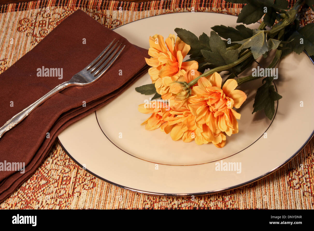 China-Teller mit Silber Gabel, braun Serviette und gelben Blumen auf einem braunen Tischset Stockfoto