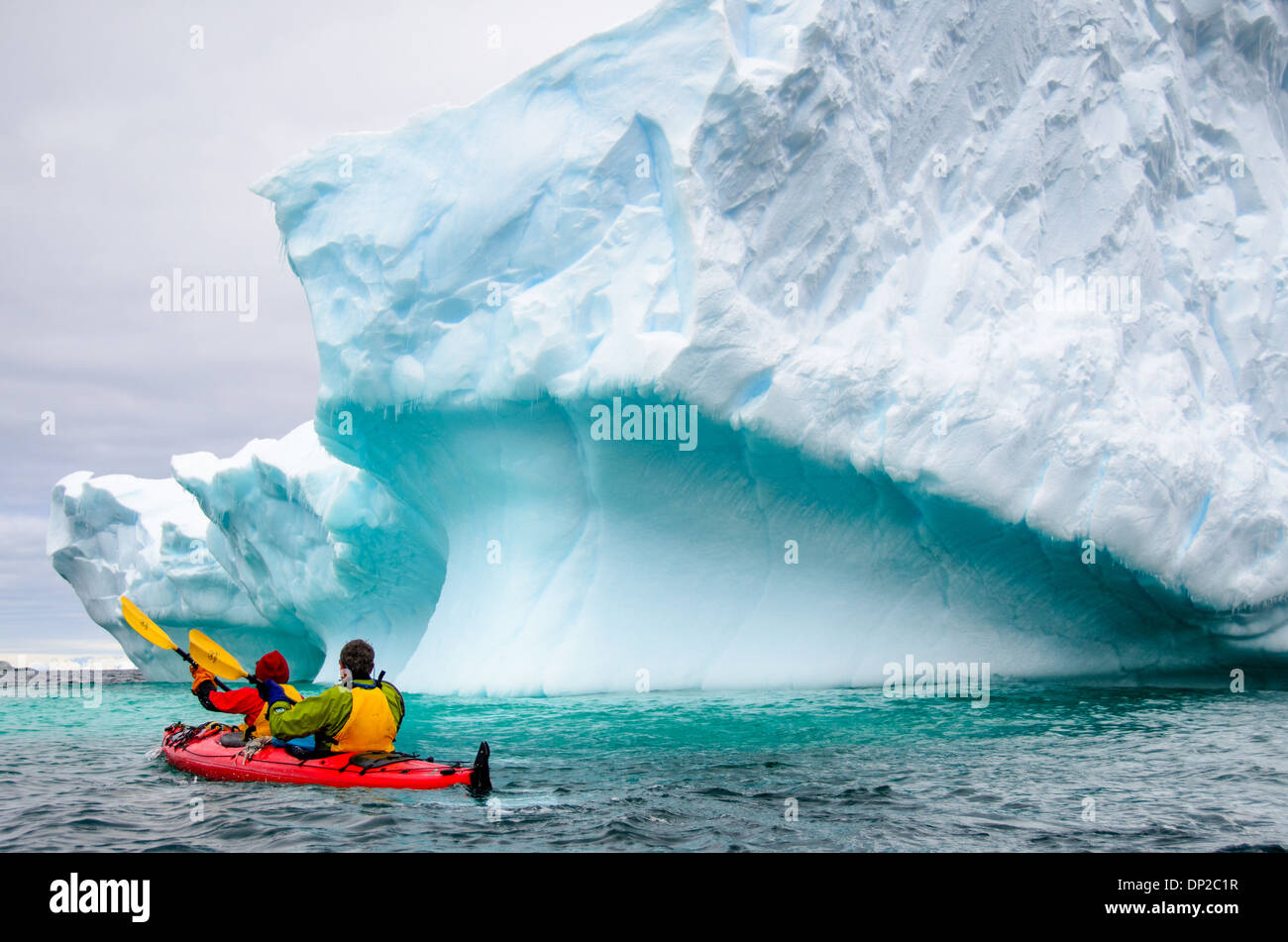 Antarktis - Kajakfahrer in einem Tandem kayak vorbei ein Eisberg, der langsam an Hydrurga Felsen an zwei hummock Insel kippen. Die Region ist bekannt als Favorit für die seeleoparden (Hydrurga leptonyx). Stockfoto