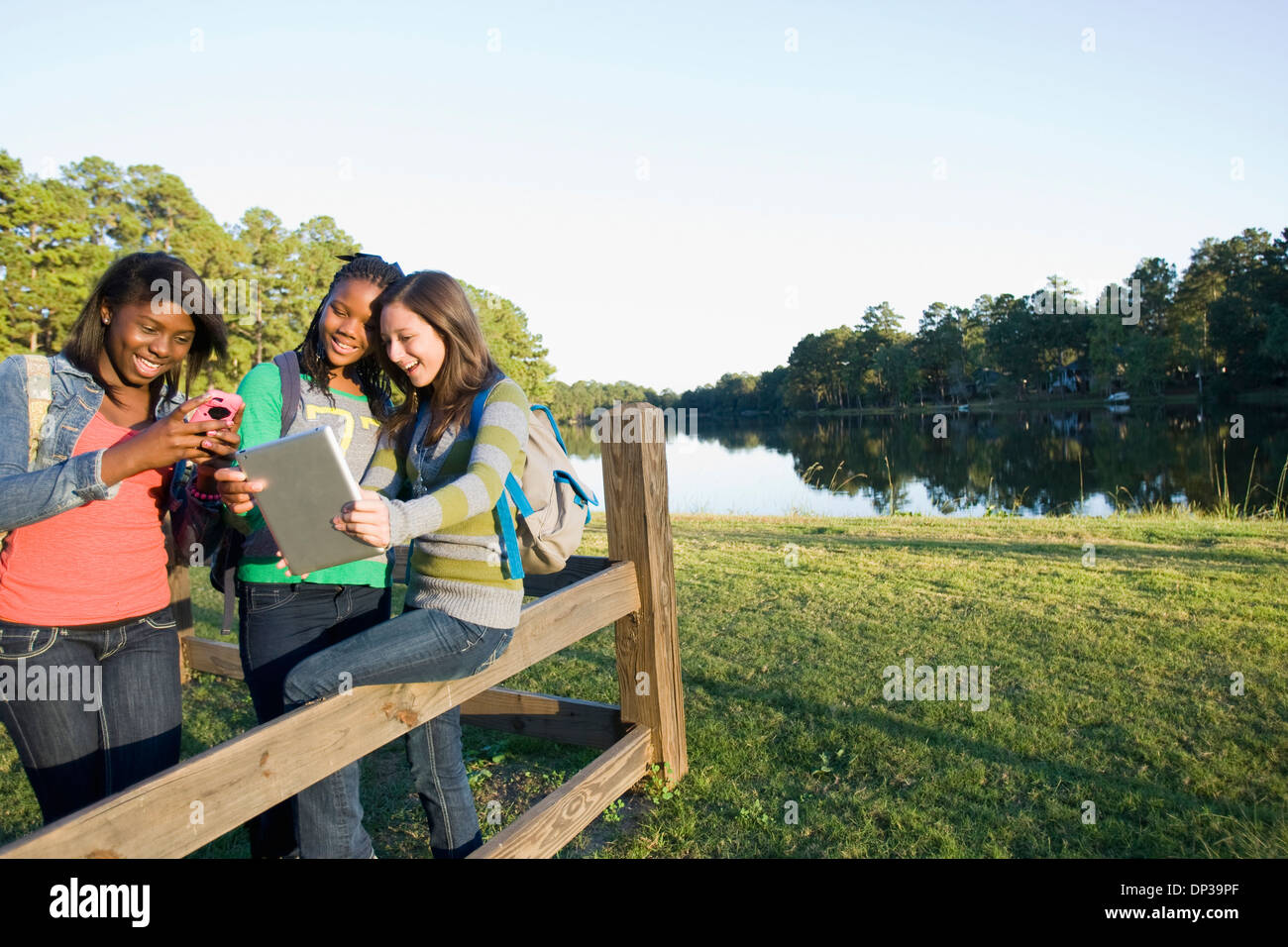 Pre-teen Mädchen sitzen auf Zaun, Blick auf Tablet-PC und Handy, im freien Stockfoto