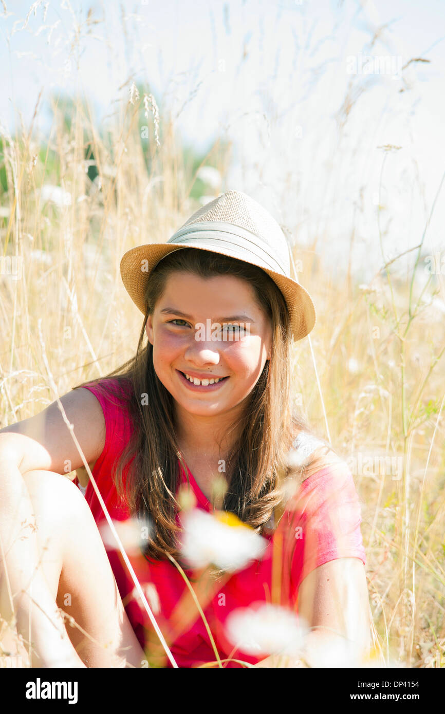 Porträt von Mädchen mit Hut, im Feld sitzen und Lächeln in die Kamera, Deutschland Stockfoto