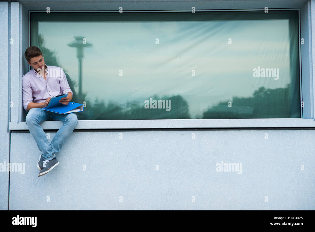 Junger Mann sitzt auf einem Felsvorsprung im Freien, Blick auf Tablet-PC, Deutschland Stockfoto