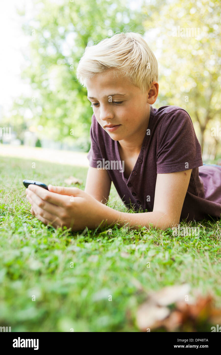 Junge liegend auf dem Rasen mit Handy, Mannheim, Baden-Württemberg, Deutschland Stockfoto