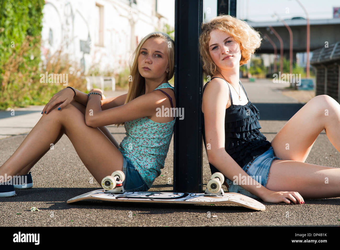 Porträt von Mädchen im Teenageralter im Freien mit Skateboard, Blick in die Kamera, sitzen auf der Straße, Deutschland Stockfoto