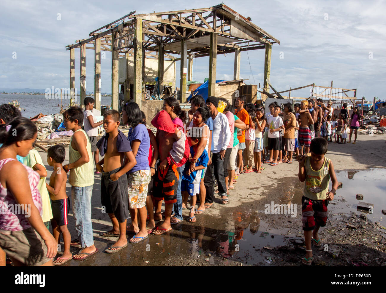 Tacloban City, Philippinen - 8. Januar 2014: 5. Januar 2014 Foto zeigt Überlebenden der Taifun Haiyan Futter für Nahrung, war im Hintergrund bleiben der ein Haus, das durch Taifun Haiyan (lokaler Name Yolanda) beschädigt wurde, schlug zentral-Philippinen letzten 8. November 2013 mehr als 6.000 Menschen getötet. Stockfoto