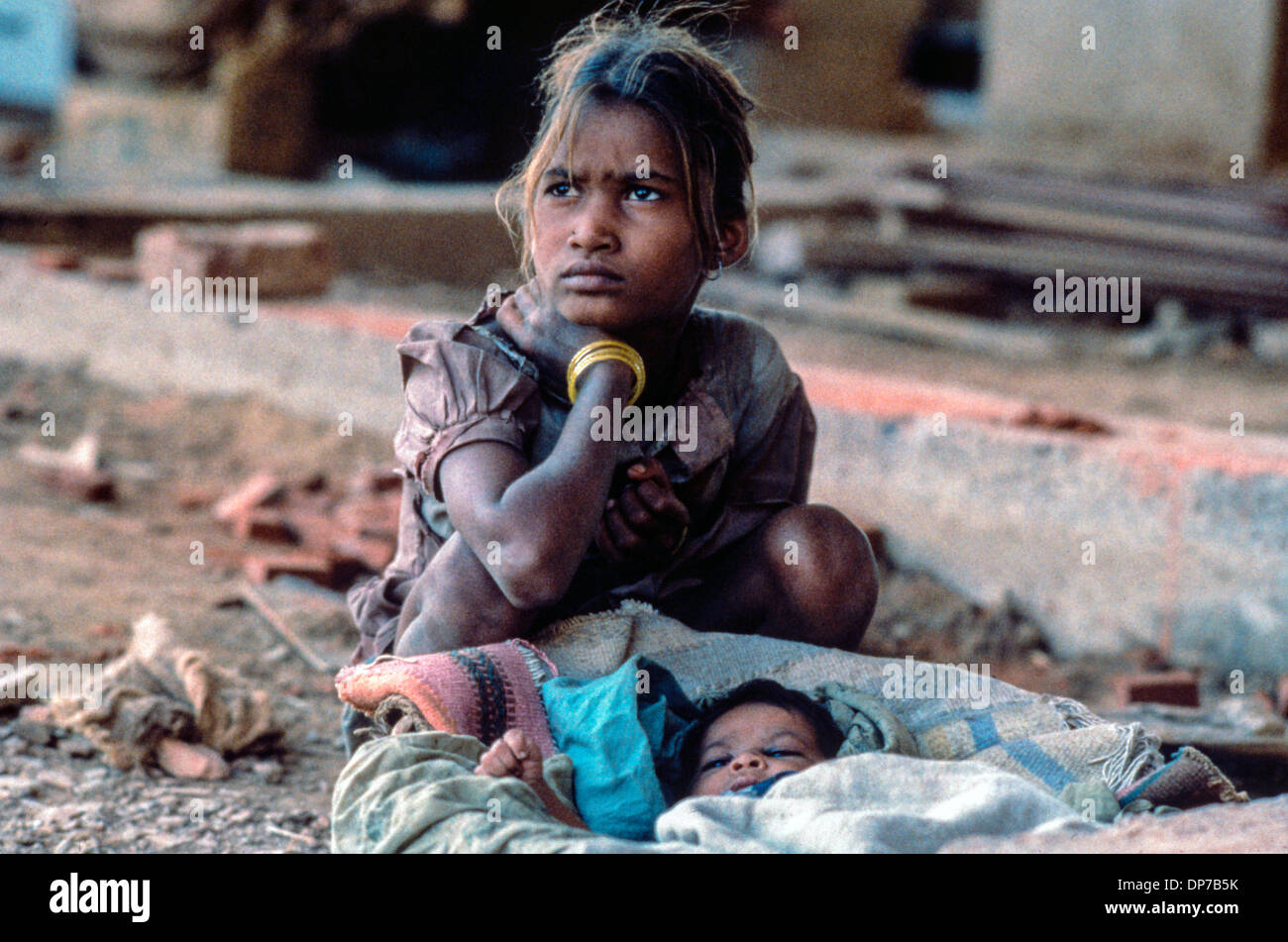Junge Mutter von niedrigen Kaste sitzt in den Trümmern & Staub einer Baustelle mit ihrem Baby in einem behelfsmäßigen Moses Korb in Delhi Stockfoto