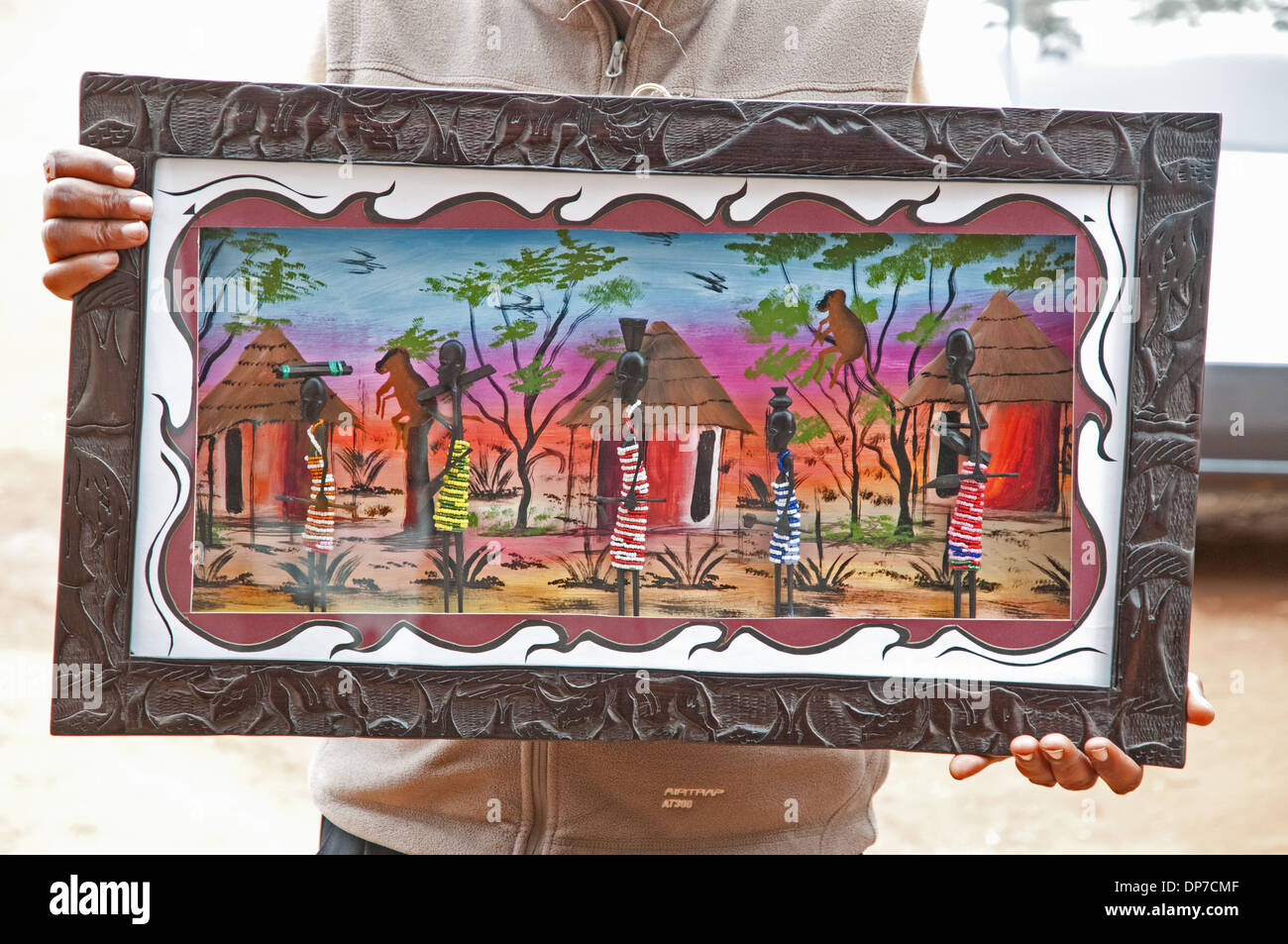 Bunte afrikanische Gemälde in geschnitzten Holzrahmen zeigt Dorf Rondavel Hütten und Frauen in traditioneller Kleidung zum Verkauf Kenia Stockfoto