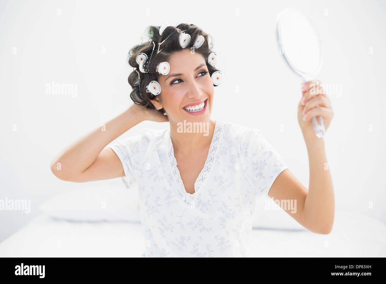 Glücklich Brünette in Lockenwickler suchen Spiegel in der hand Stockfoto