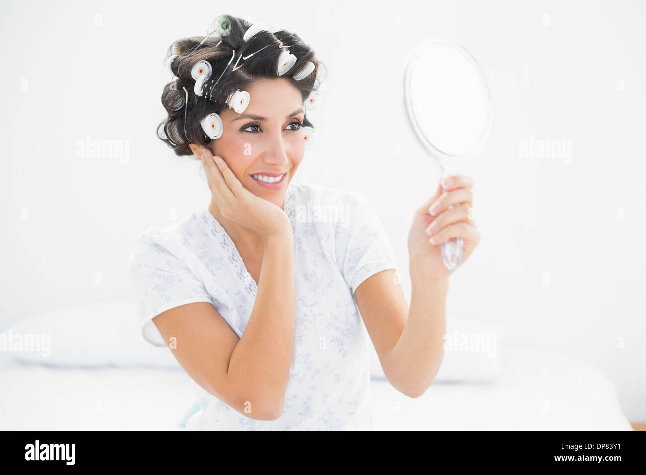 Hübsche Brünette in Lockenwickler suchen Spiegel in der hand Stockfoto