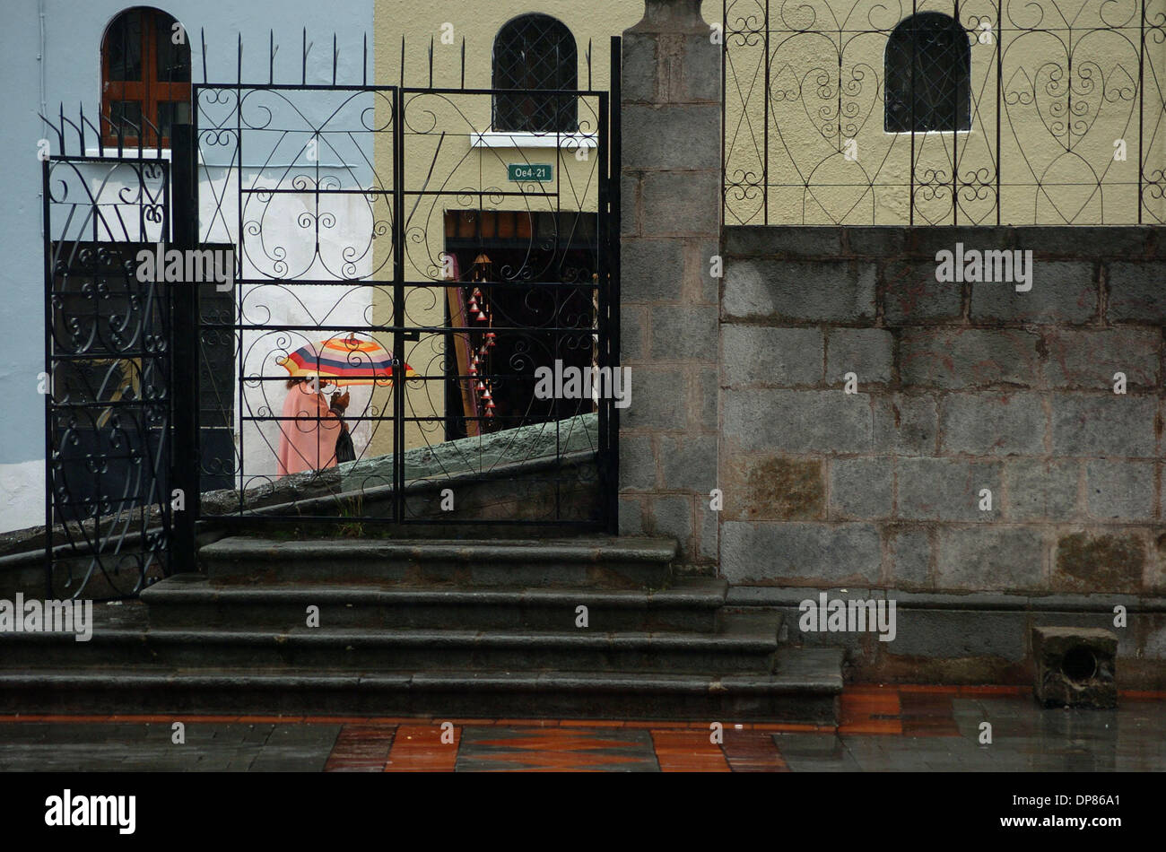 7. November 2006 - Quito, Ecuador - eine Frau in rosa gekleidet und trägt einen lebhaft gefärbten Regenschirm geht vorbei an schwarzen Metall und graue Pflastersteine, die das Tor zu der Basilika del Voto Nacional in Ecuadors Hauptstadt bilden. Auf einem kleinen Hügel in der Altstadt Quitos und sichtbar von einem Großteil der Stadt befindet, sich die neugotische Kirche, gebaut im Jahre 1892 eines der ältesten kolonialen build Stockfoto