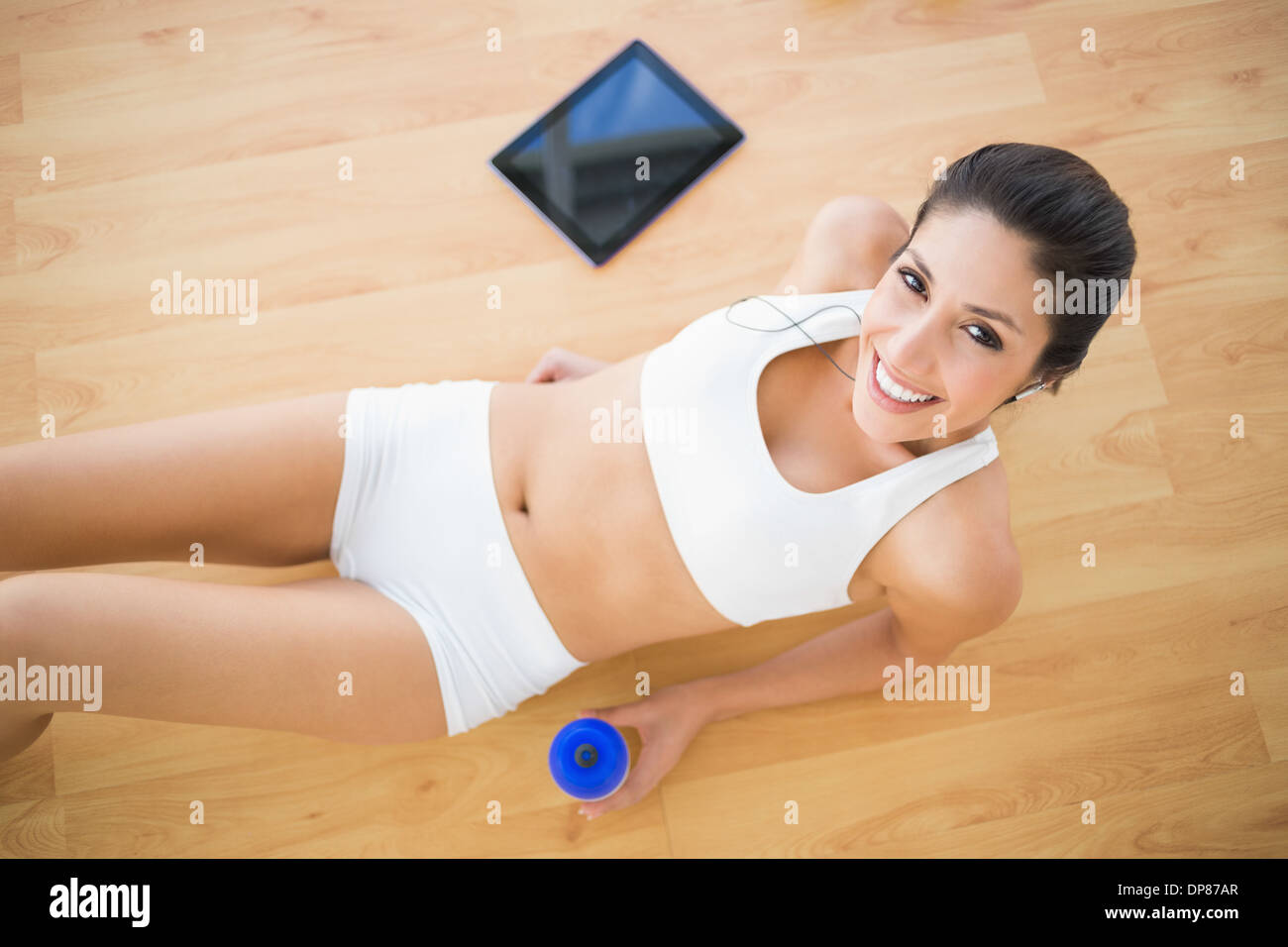 Fit lächelnde Frau hält Sportflasche liegend auf Holzboden Stockfoto