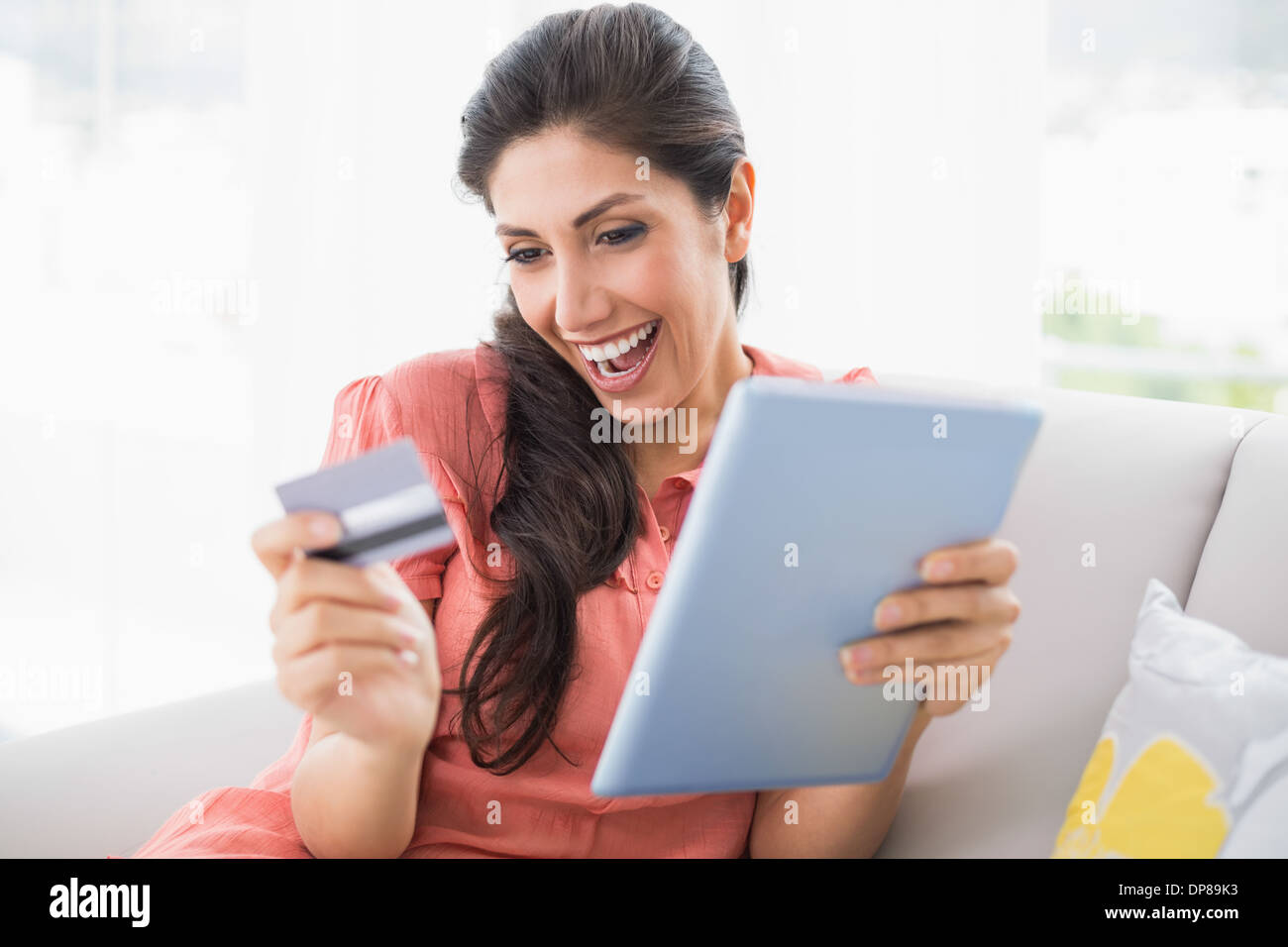 Aufgeregt, Brünette sitzen auf ihrem Sofa mit Tablet Shop online Stockfoto