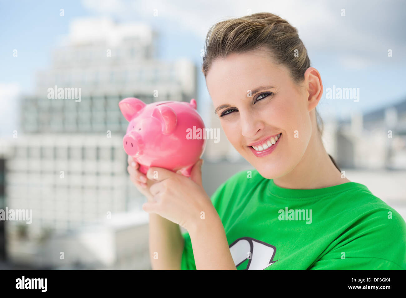 Lächelnde Frau tragen grüne recycling Tshirt mit Sparschwein Stockfoto