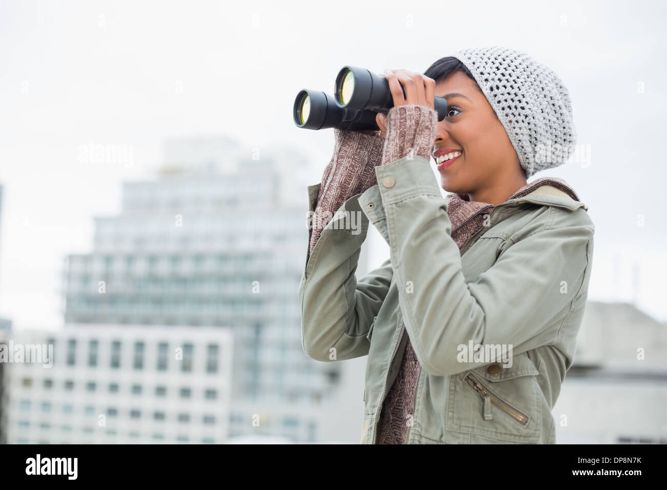 Lächelnde junge Modell in Winterkleidung beobachten mit dem Fernglas Stockfoto