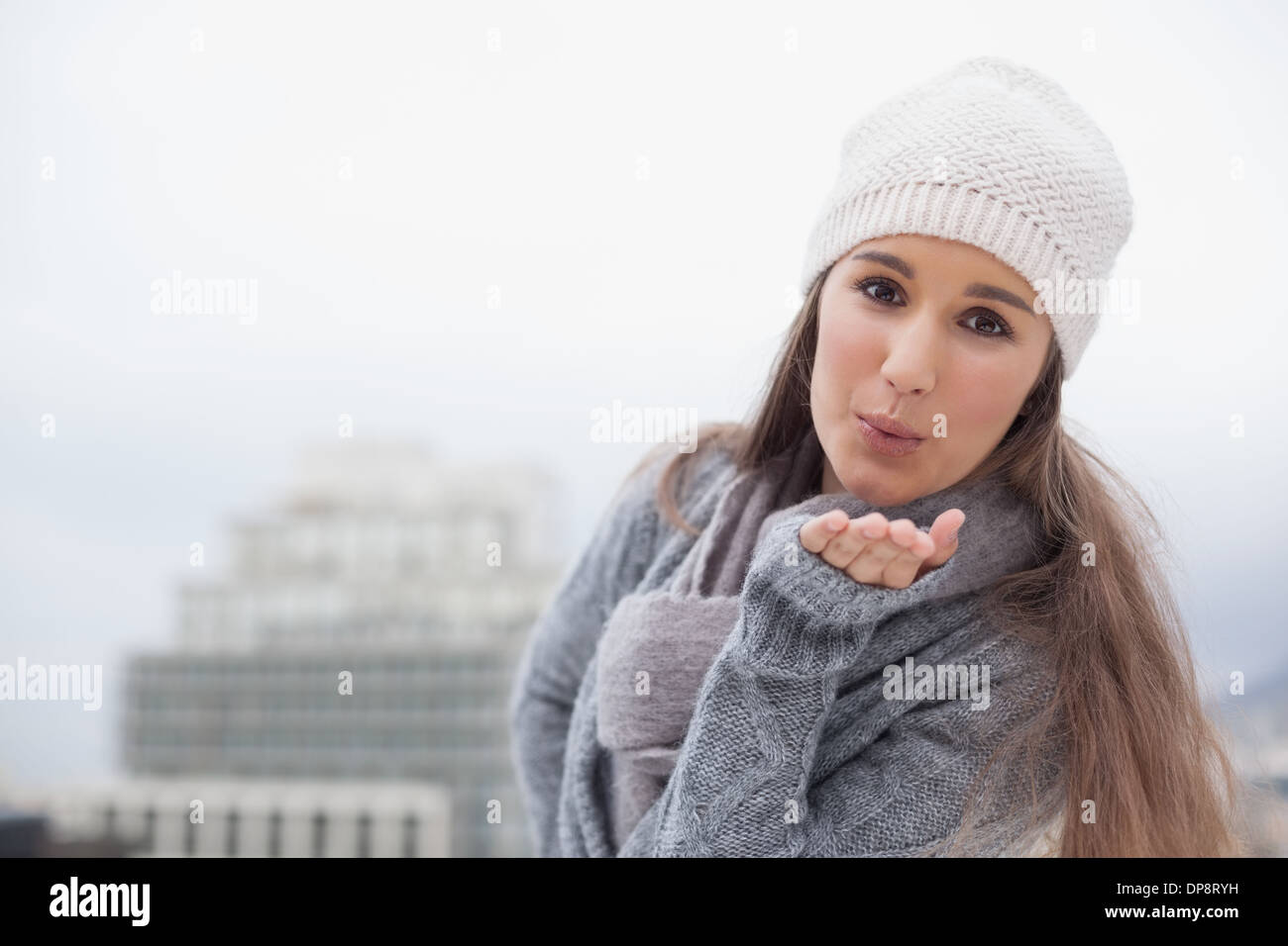 Hübsche Brünette mit Winterkleidung zum Senden eines Luft-Kuss an Kamera Stockfoto