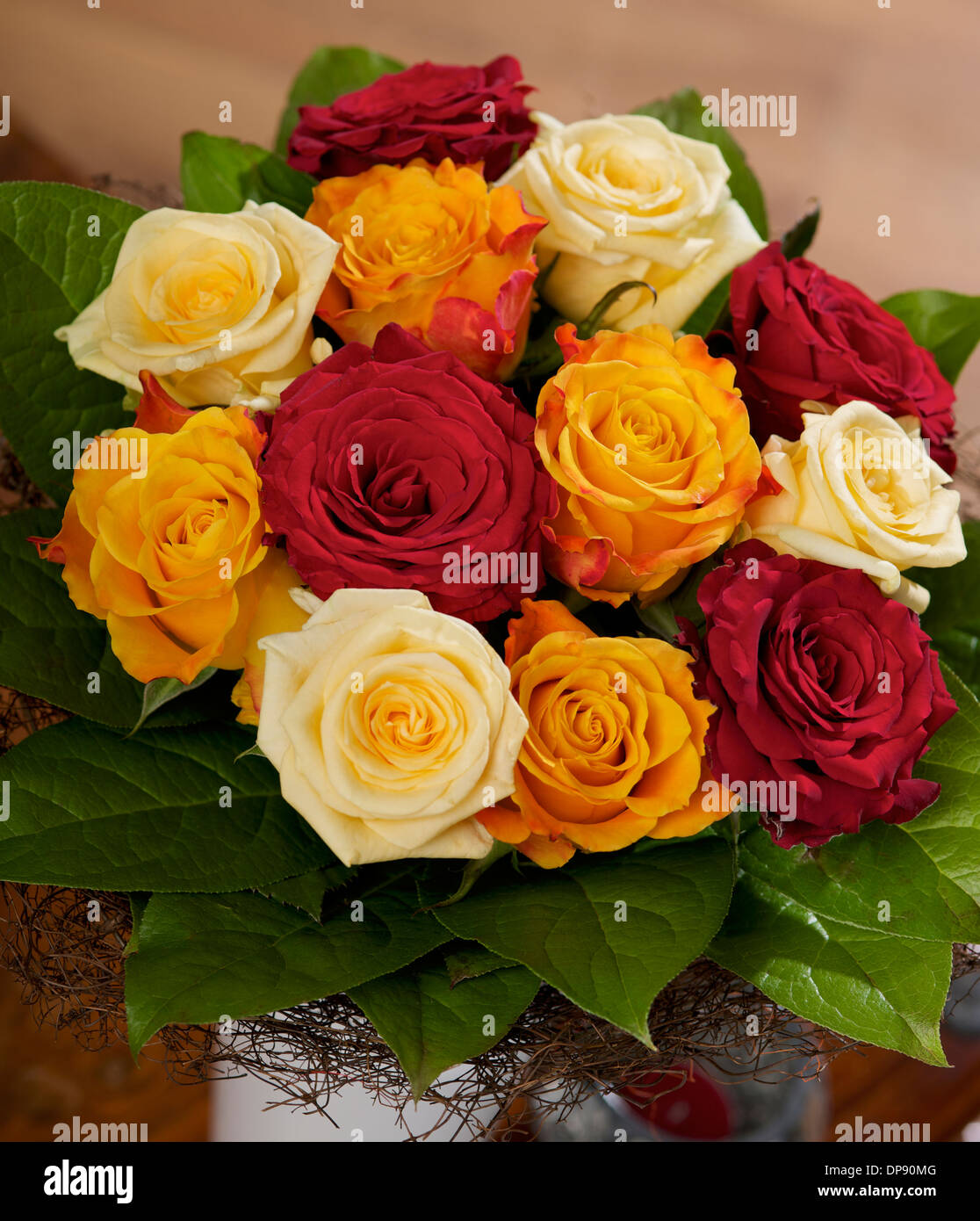 Bouquet von Creme-, Rot- und Orangenrosen mit Salalblatt der Marie Claire Rose in Vase auf einem Tisch in häuslicher Umgebung Stockfoto