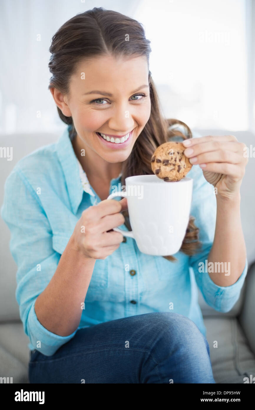 Lächelnde Frau eintauchenden Cookie in Kaffee Stockfoto