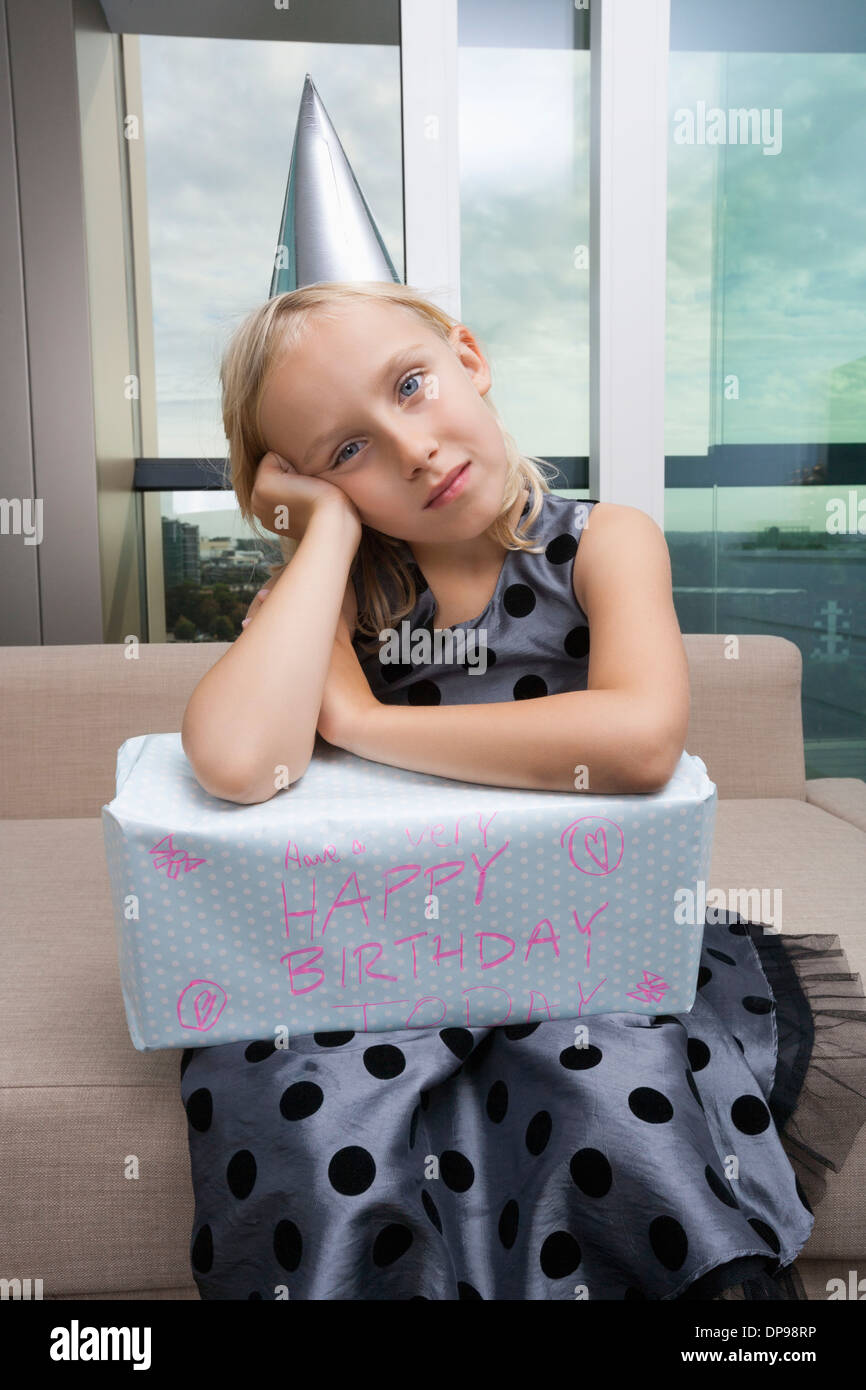 Porträt von trauriges Mädchen mit Geburtstagsgeschenk sitzt zu Hause auf sofa Stockfoto