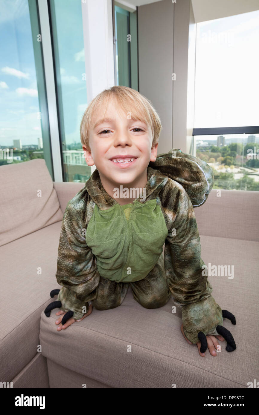 Porträt von fröhlicher Junge Dinosaurier Kostüm zu Hause auf Sofa kniend Stockfoto