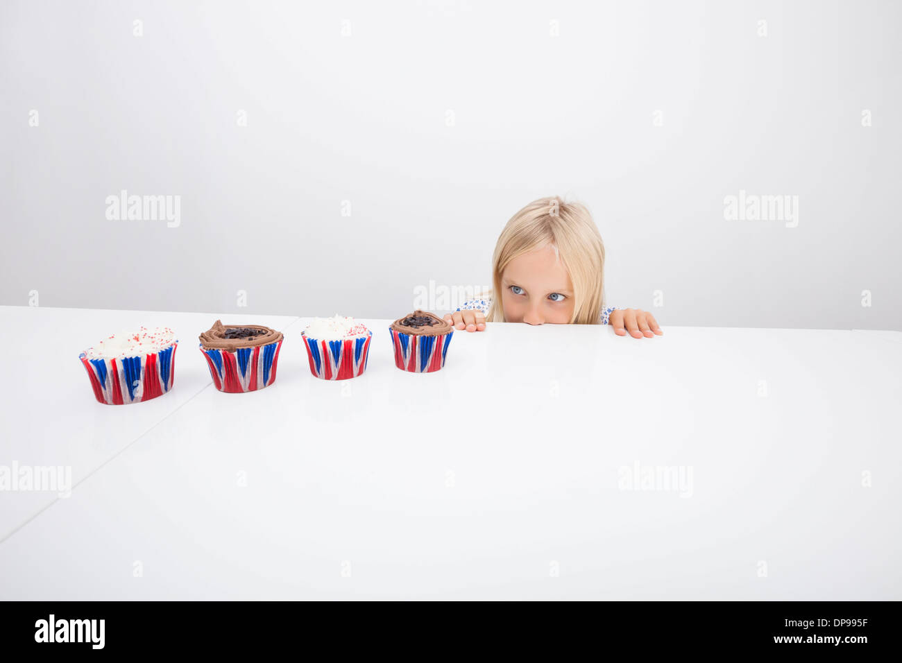 Versucht Mädchen starrte auf Cupcakes auf Tisch Stockfoto