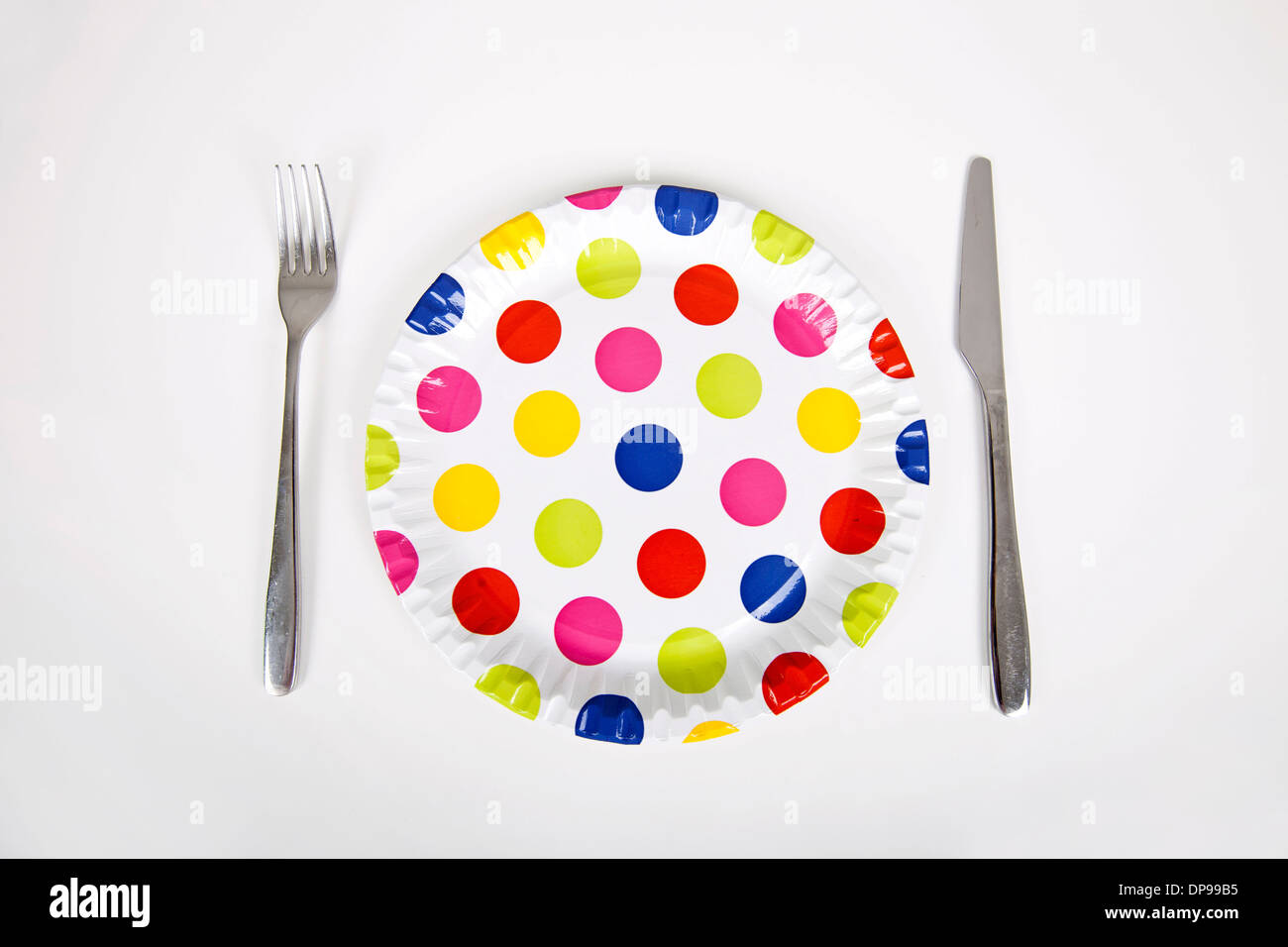 Bunte Platte mit Polka Dots und Besteck vor weißem Hintergrund Stockfoto