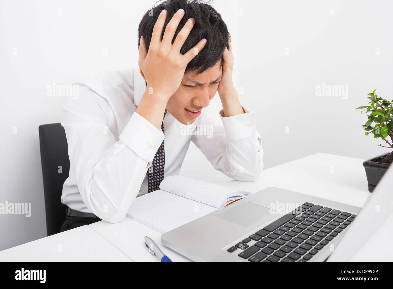 Frustriert Geschäftsmann mit Kopf in Händen sitzen am Schreibtisch im Büro Stockfoto