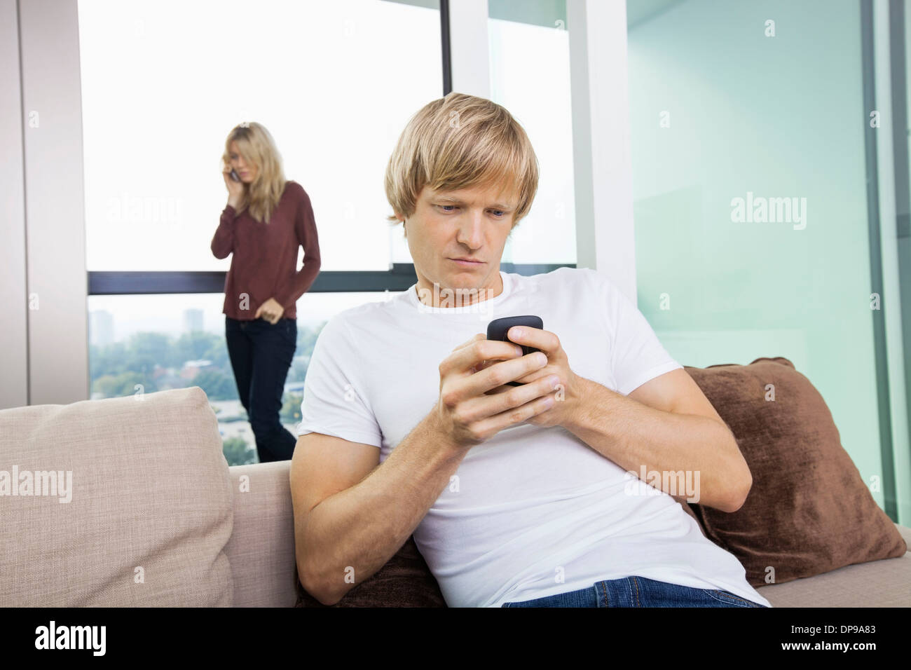 Mid-Adult Mann SMS während Frau mit Handy im Hintergrund zu Hause Stockfoto