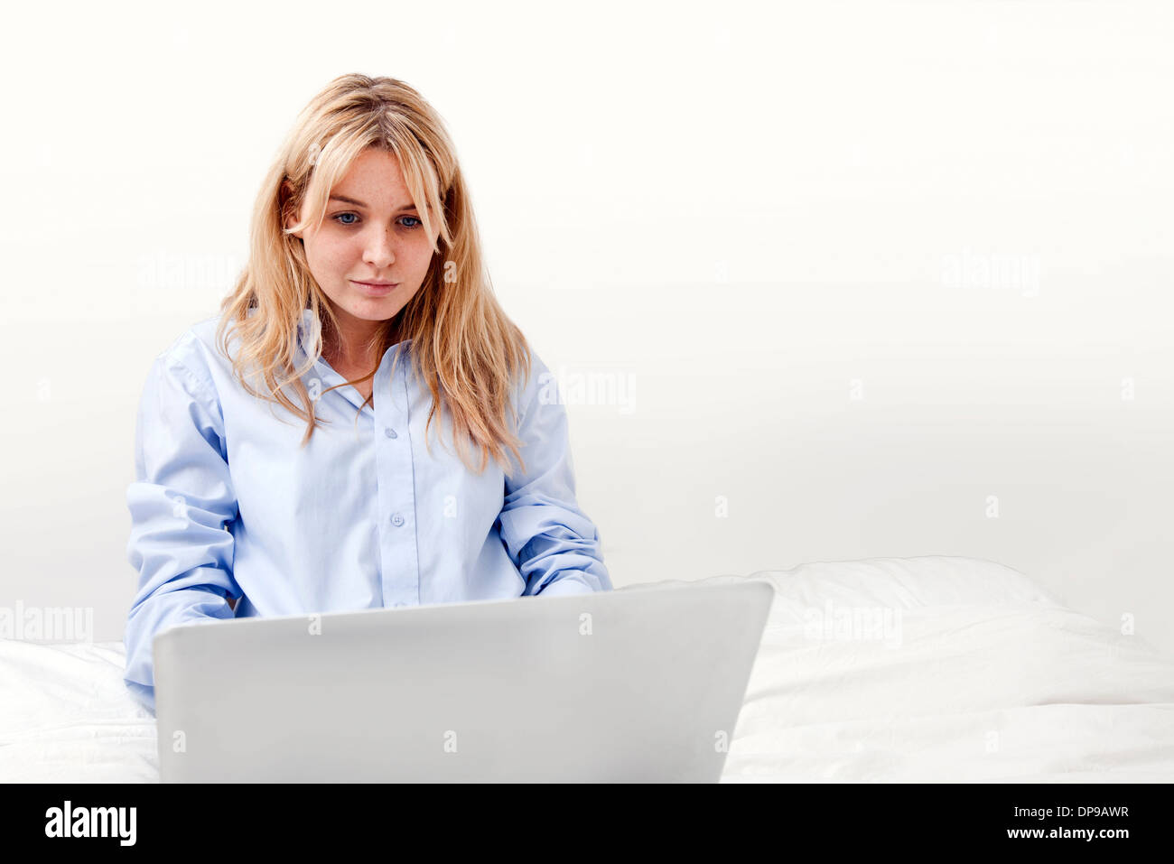 Junge Geschäftsfrau mit Laptop im Bett Stockfoto