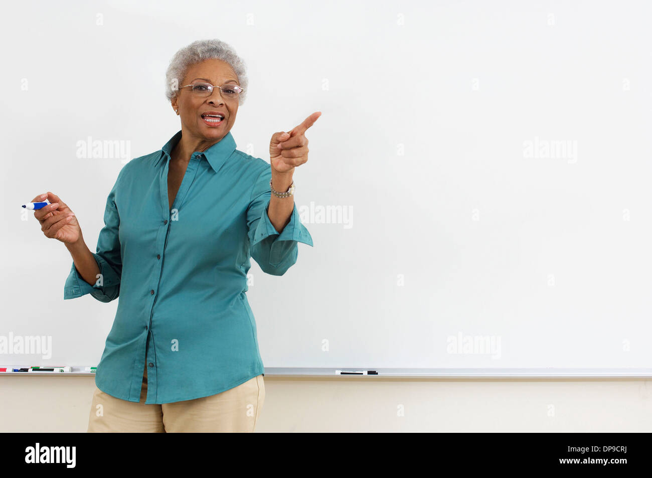 Oberlehrer zeigt beim gestikulieren gegen weiße Tafel im Klassenzimmer Stockfoto