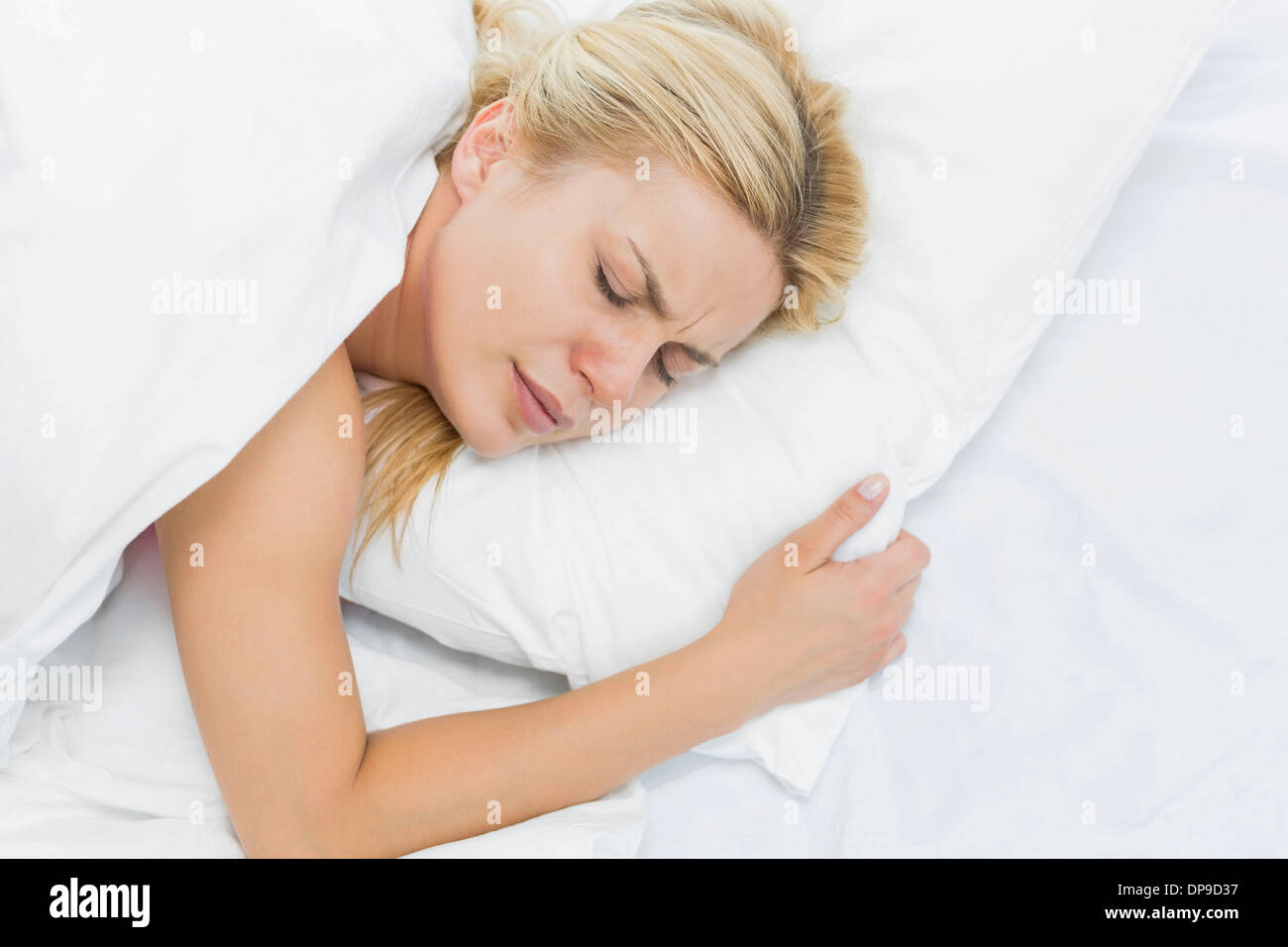 Junge Frau vor Schmerz auf Bett liegend Stockfoto