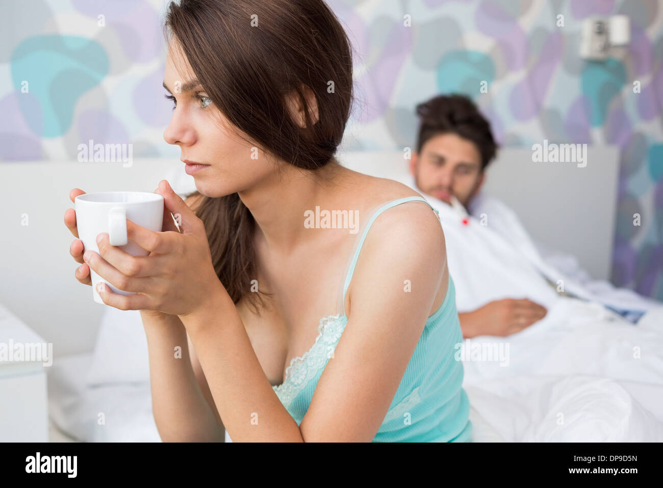 Besorgt junge Frau mit Kaffeetasse und kranker Mann entspannend im Hintergrund Stockfoto